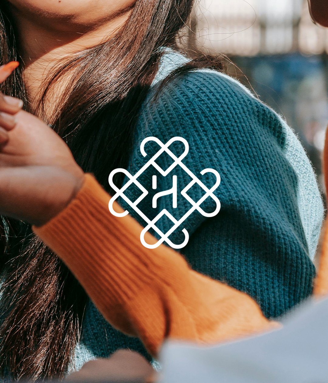 Close-up of a person wearing a teal sweater and orange sleeves, with hair visible, featuring a white geometric logo overlay.