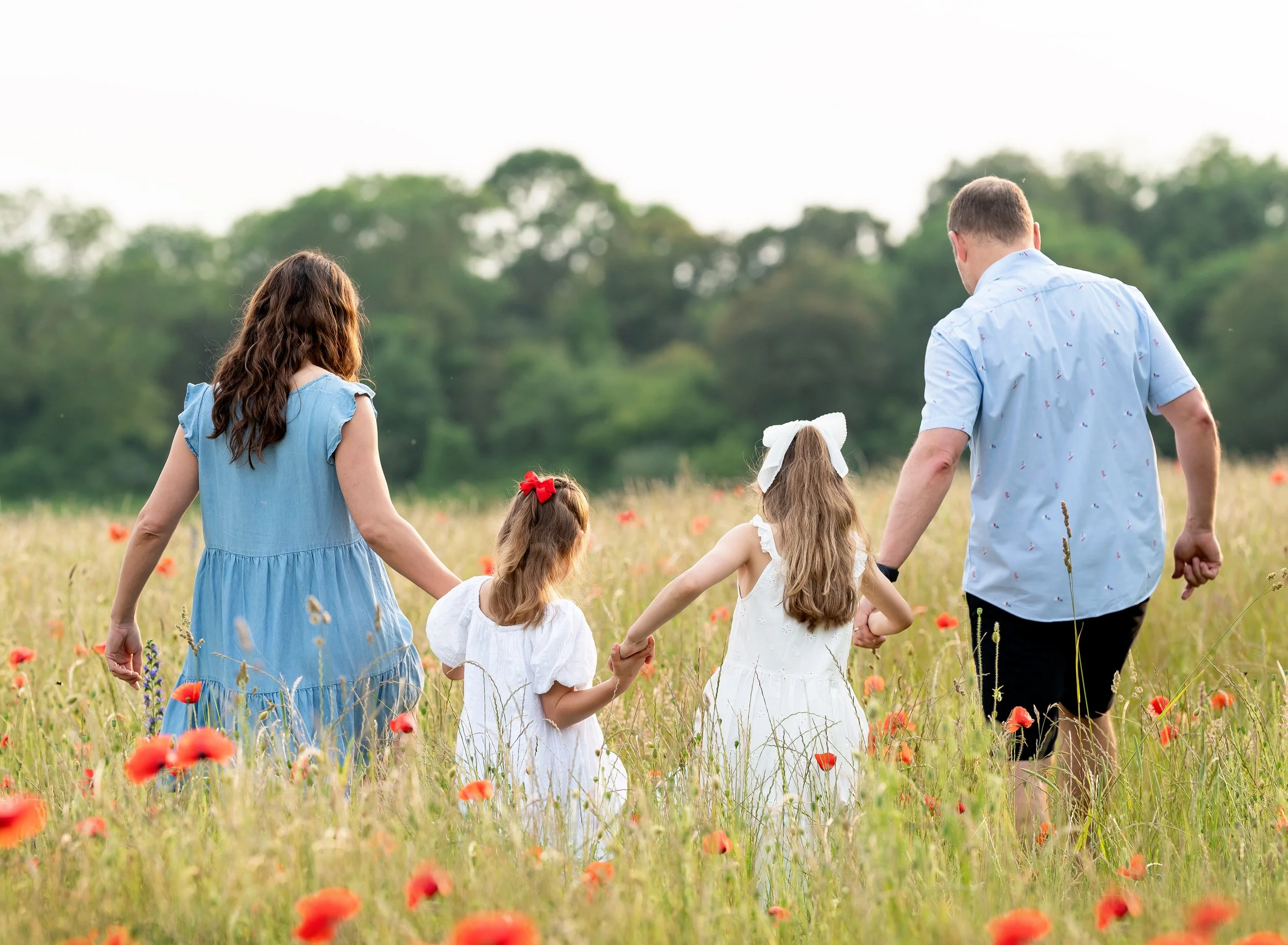 Family of four walking through a meadow with orange flowers, holding hands, with trees in the background.