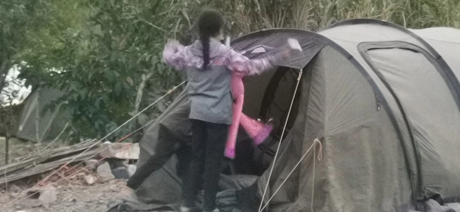 A person setting up or interacting with a large camping tent outdoors, surrounded by trees and natural terrain.