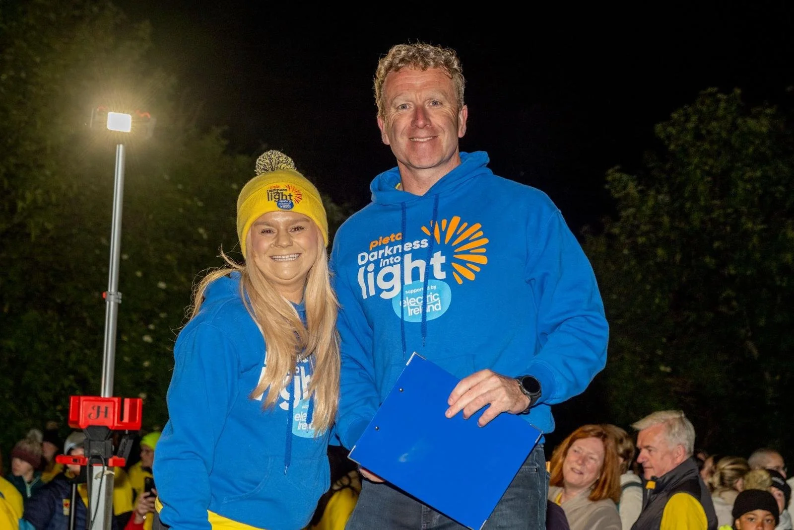 Two people a man and a woman standing in dark for Darkness into light 2026 mental health community event