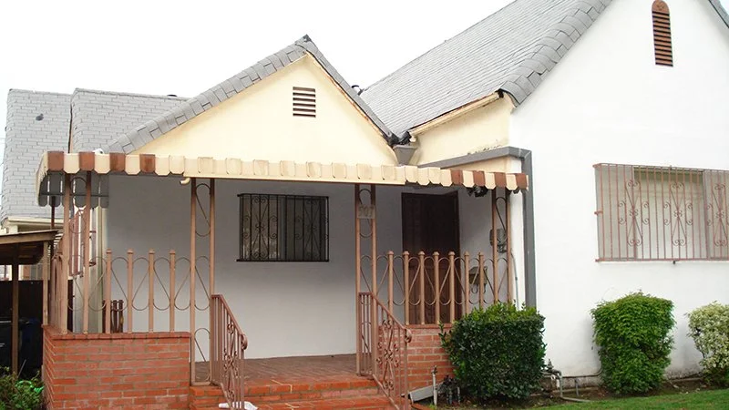 Front view of a house with a small porch, brick stairs, and metal railings, surrounded by bushes.