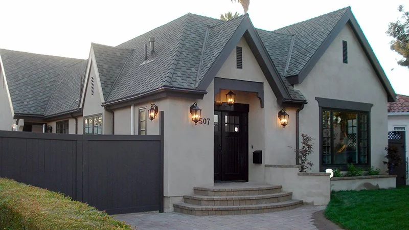 A modern house with a steep gray roof, light exterior walls, black front door, and lantern-style outdoor lighting.