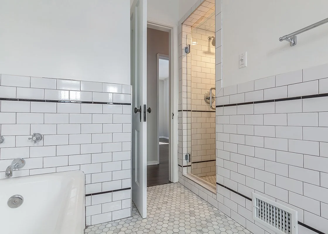 Bathroom with white subway tile walls, hexagonal floor tiles, a bathtub, and a separate shower stall, with a door leading to another room.