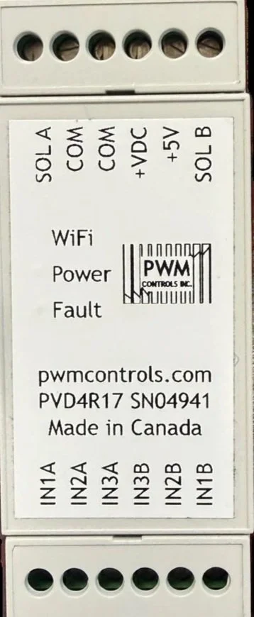 Close-up of an electronic device with multiple labeled connection ports and status indicators. Labels include SOLA, COM, +VDC, +5V, B, IN1A, IN2A, IN3A, IN3B, IN2B, IN1B, WiFi, Power, Fault, and a barcode with PWMC controls.