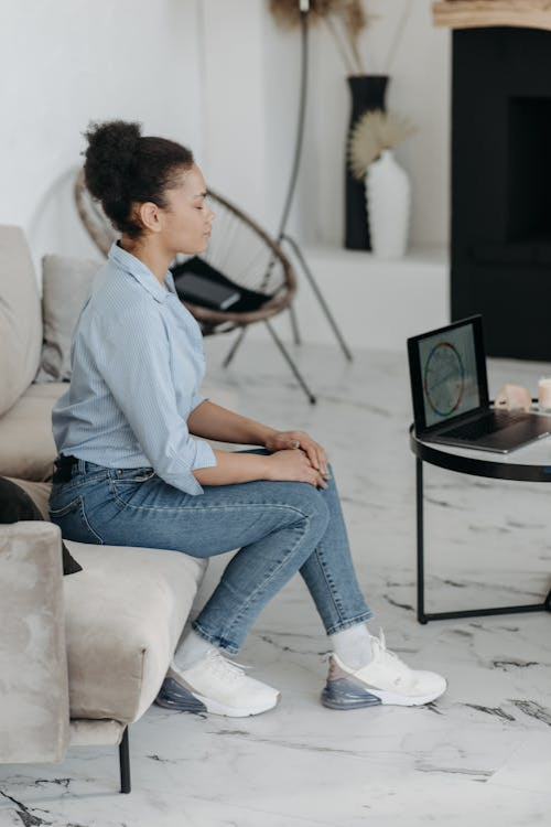 Young woman sitting on a beige sofa watching a laptop displaying a colorful graph in a modern living room.