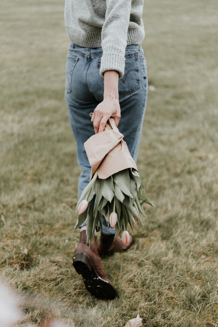 Person walking on grass holding a bouquet of pink tulips wrapped in paper.