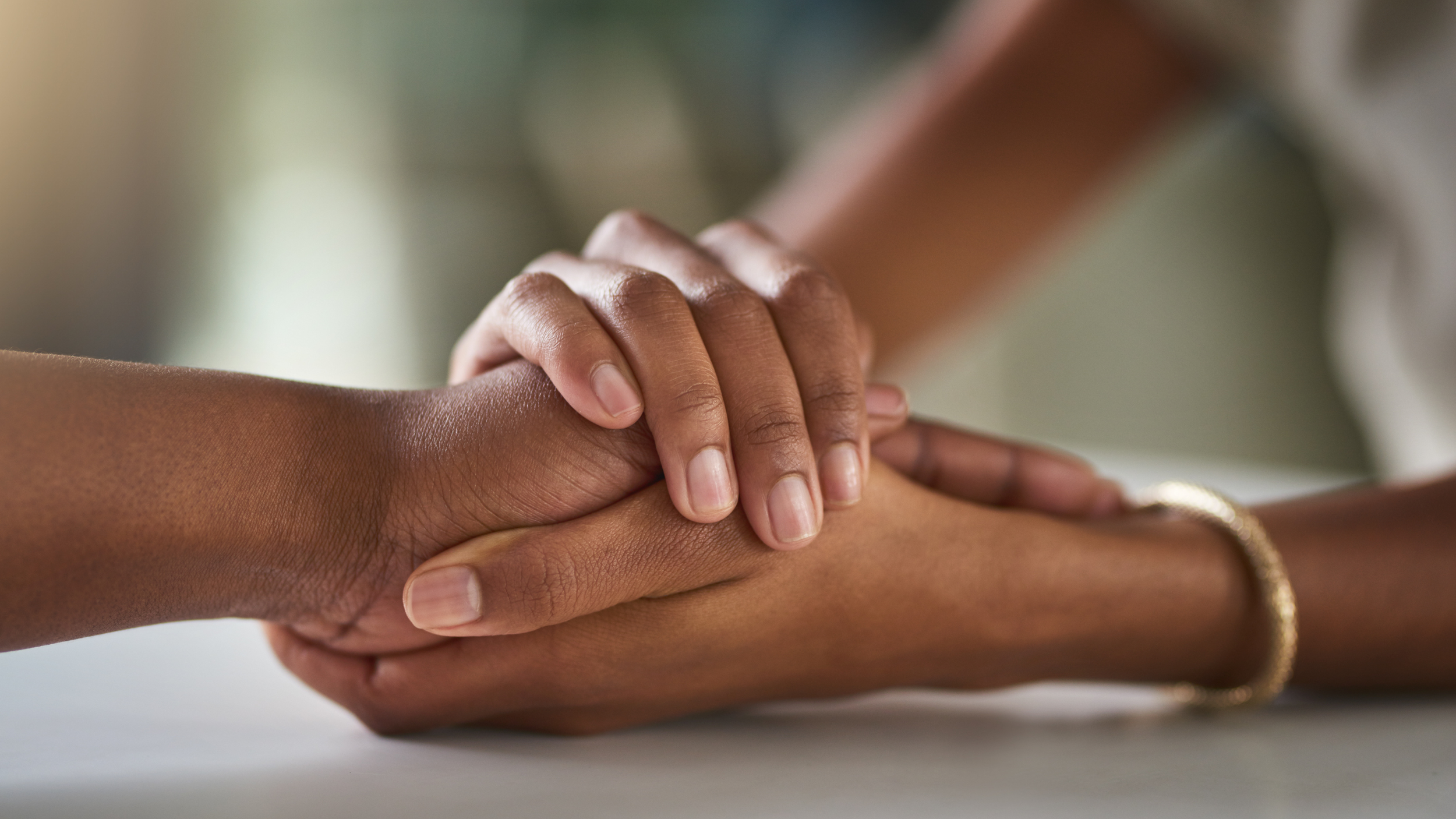 Two women holding hands gently, with one hand resting on top of the other, sharing a moment of connection.