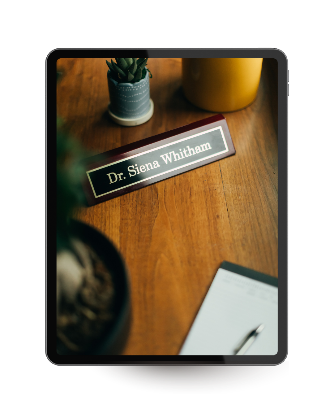 Close-up of a nameplate reading 'Dr. Siena Whitham' on a wooden desk, with potted plants and a notepad nearby.