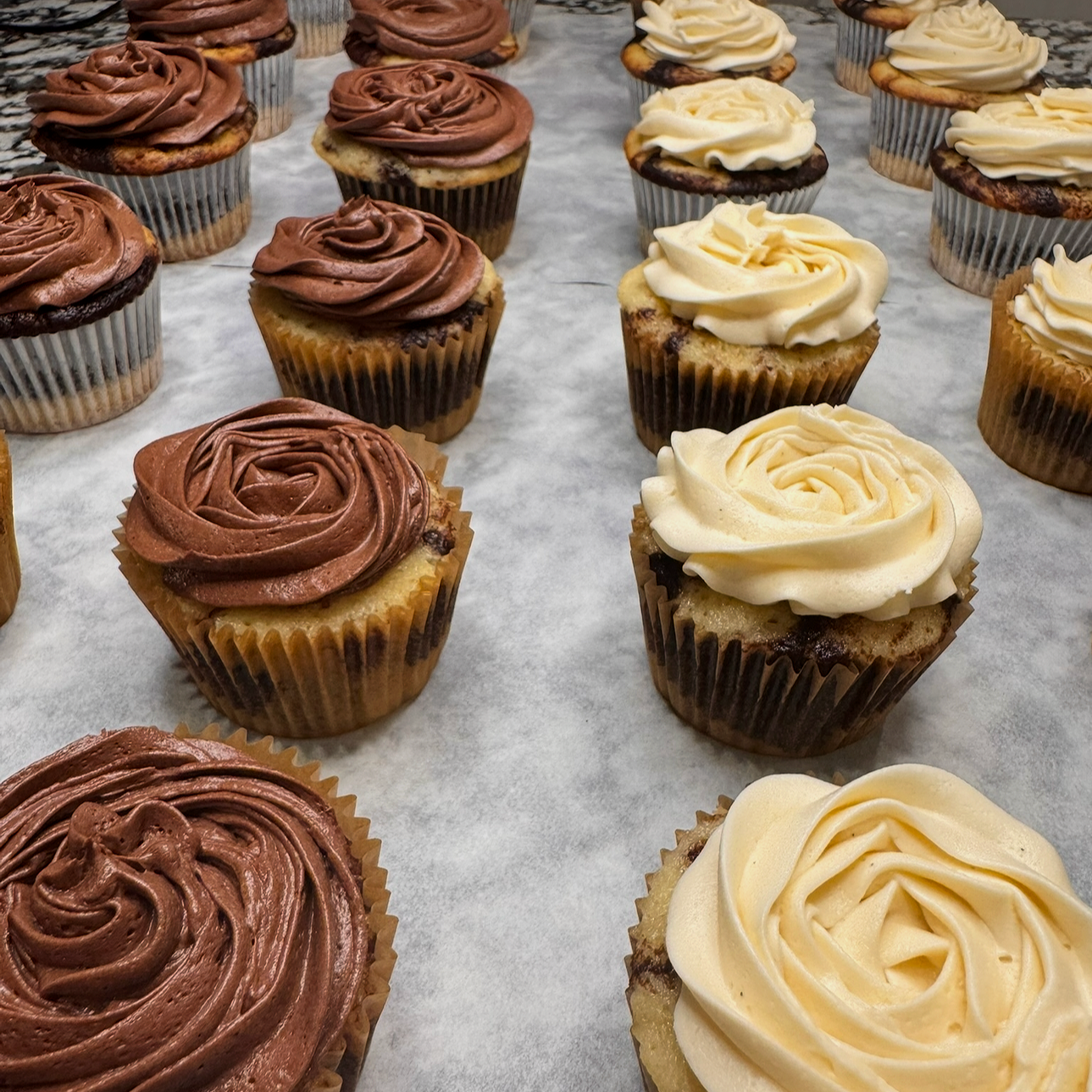 Assorted cupcakes with chocolate and vanilla frosting on a parchment-lined surface.