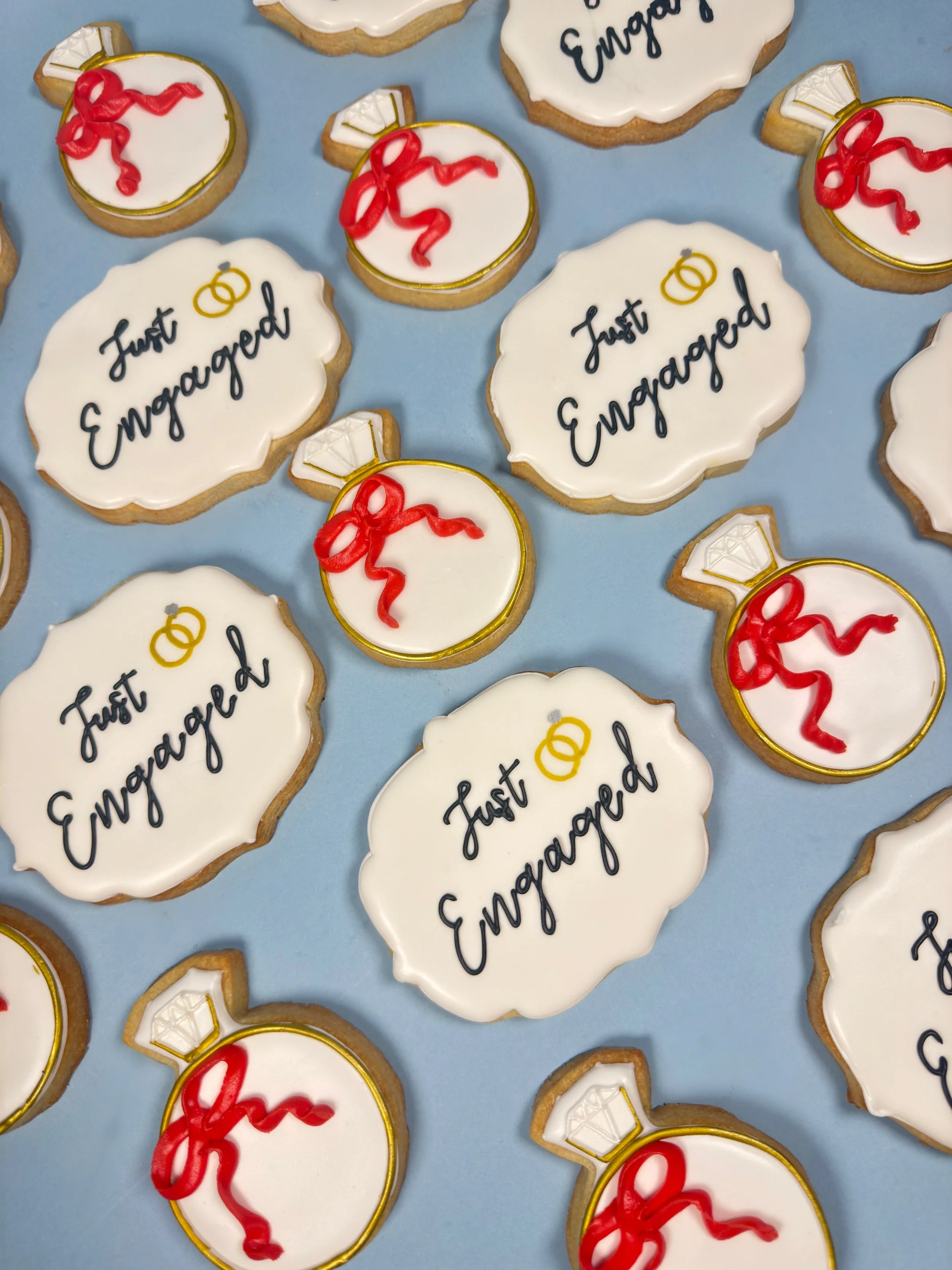 Cookies decorated with wedding theme, including rings, slogans, and gift box designs, on a blue background.