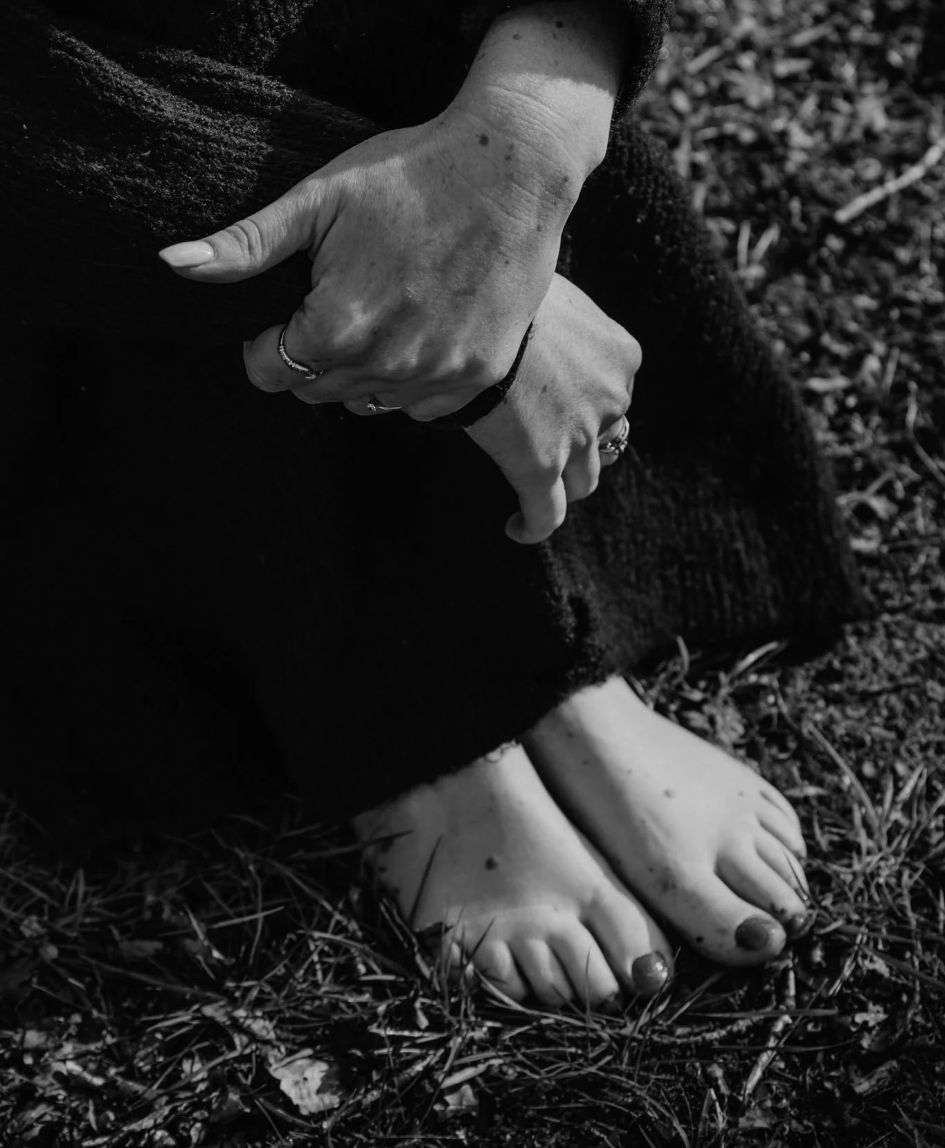 Zwarte en witte foto van een persoon met blote voeten op gras, terwijl ze op haar knie leunt en haar handen op haar knie plaatsen.