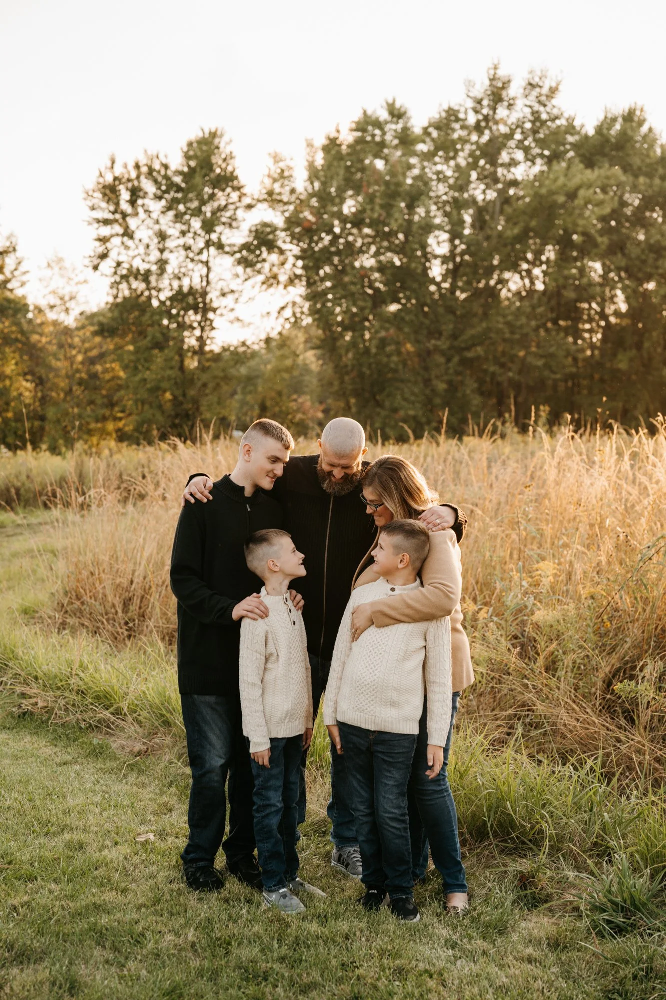 Family of six standing together outdoors during sunset, hugging and smiling.