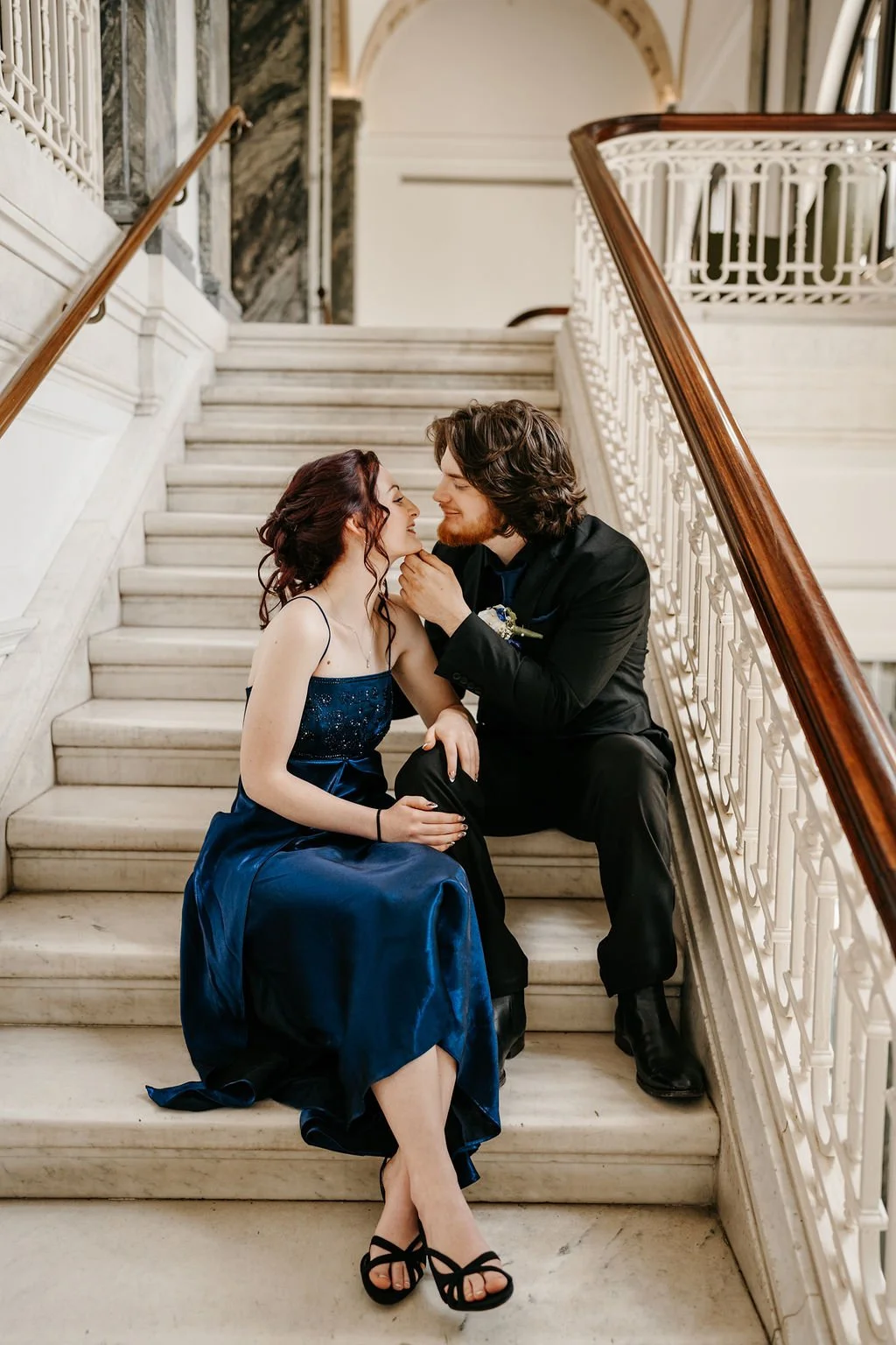 A young couple sitting on a staircase, gazing lovingly at each other, with the man gently touching the woman's face.