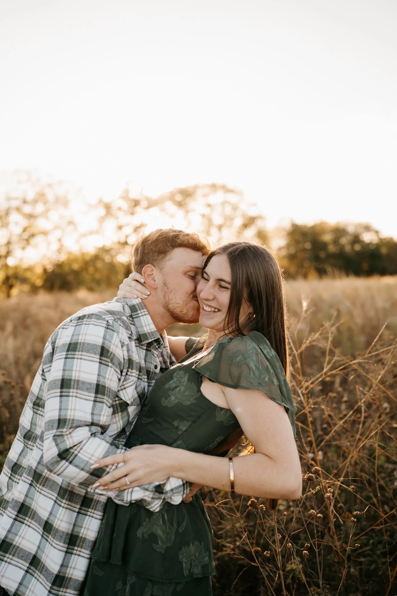 A joyful couple embracing in a field during sunset, smiling and sharing an intimate moment.