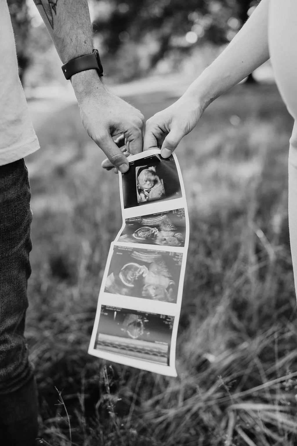 Two people holding ultrasound images of a baby outdoors.