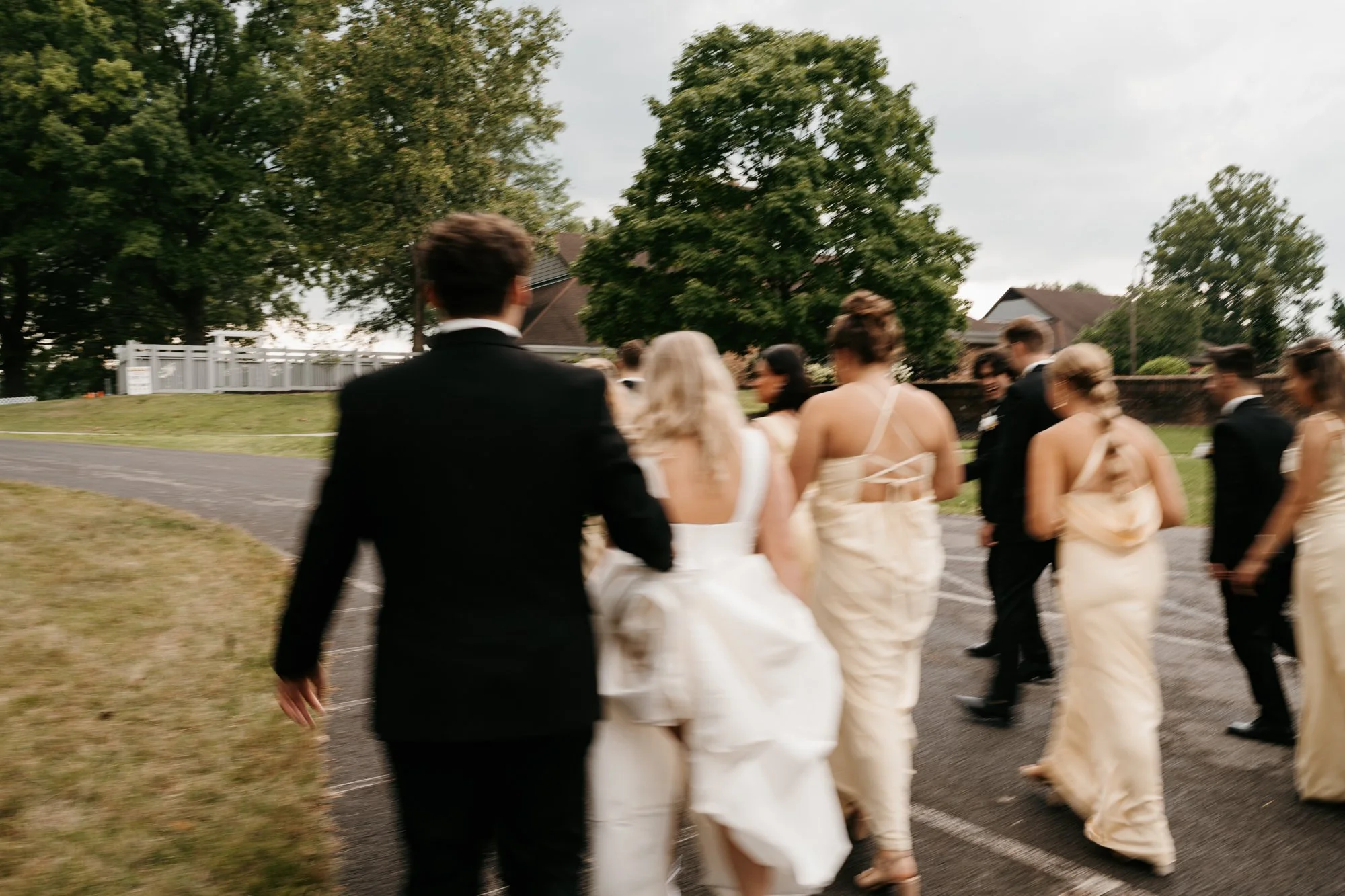 Group of people dressed in formal attire walking outdoors on a cloudy day.