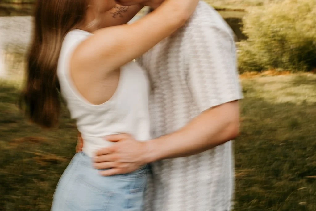 A close-up of a couple hugging outdoors, with the woman's arm around the man's neck and the man's arms around her waist.