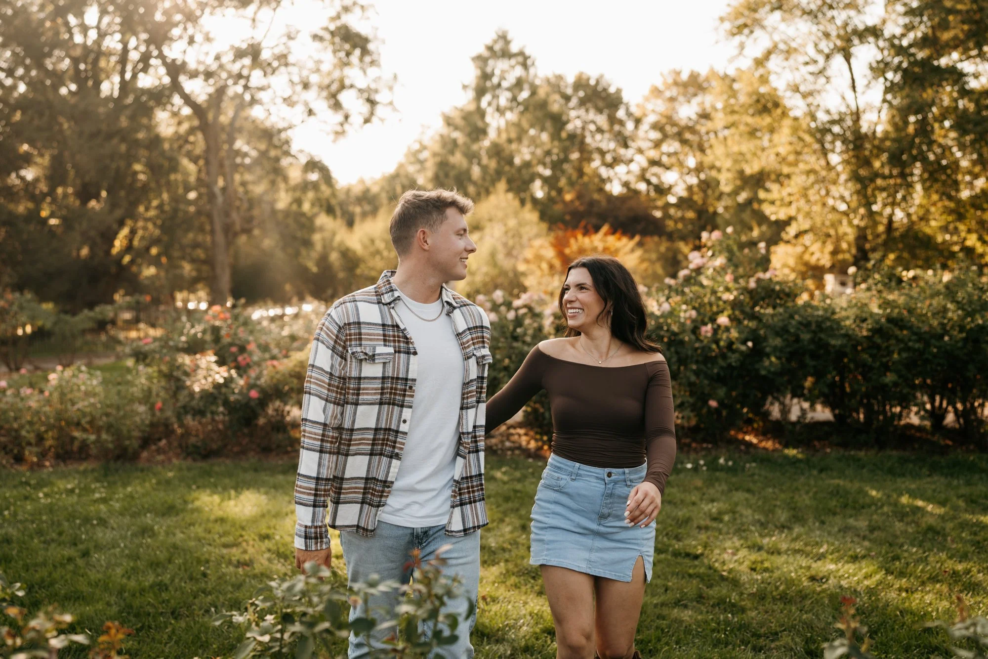 A young couple walking together in a park during sunset, smiling and looking at each other.
