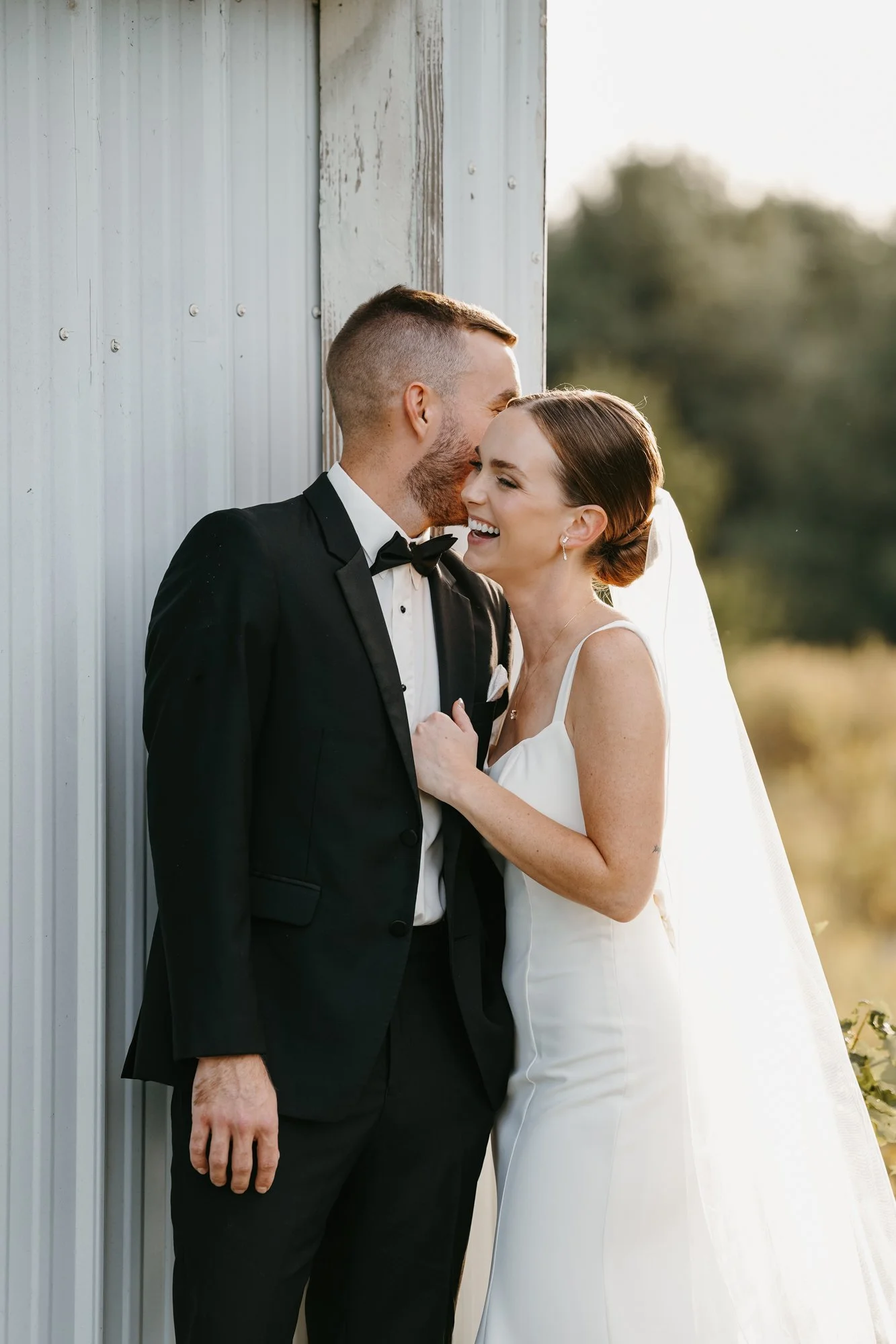 A happy bride and groom in wedding attire sharing a laugh outdoors.