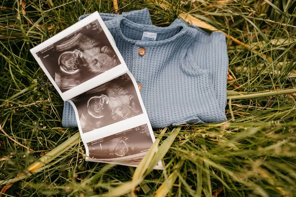 Blue baby onesie laid on grass with ultrasound images nearby.