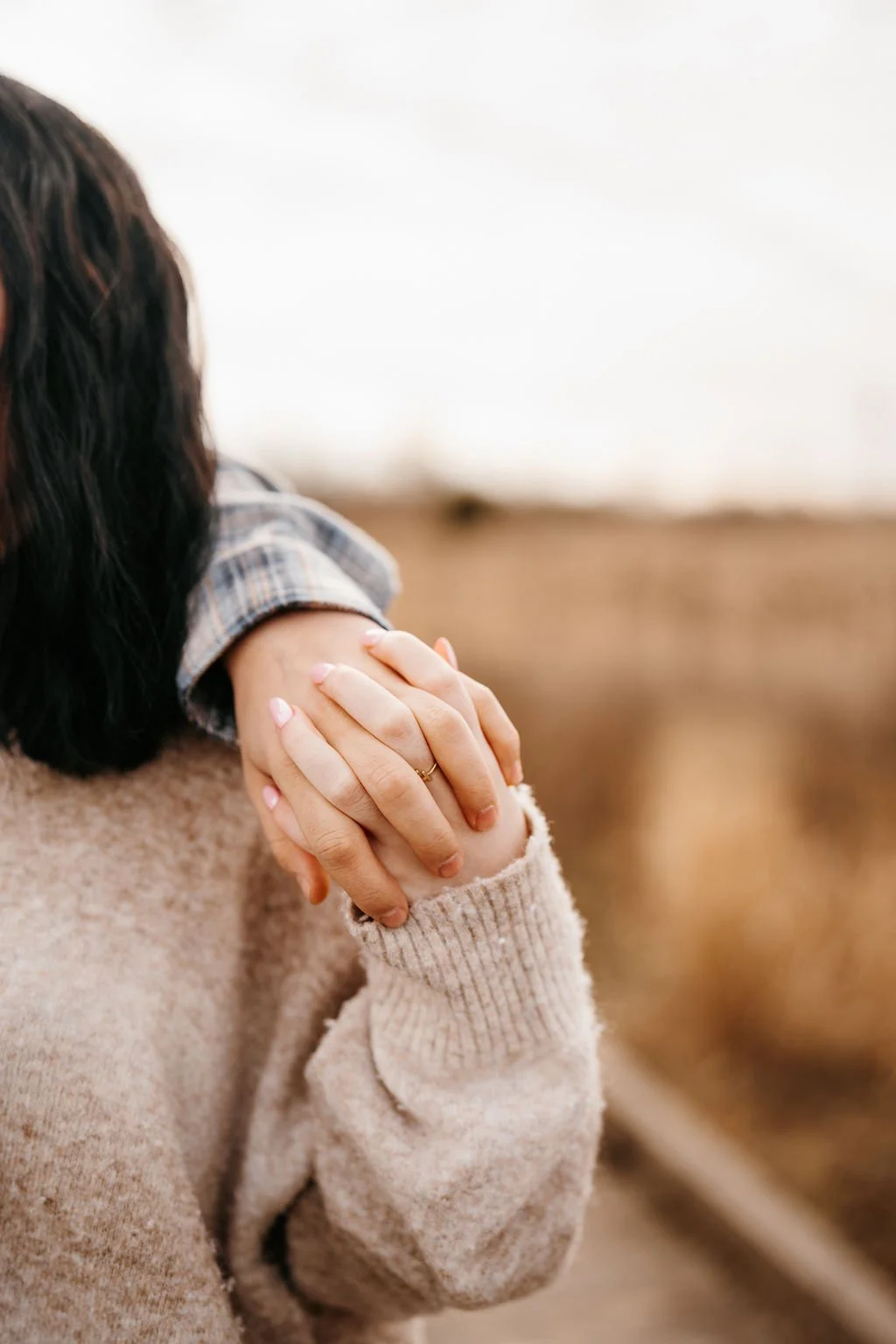Two people holding hands, one resting on the other's shoulder, in a warm, cozy setting.