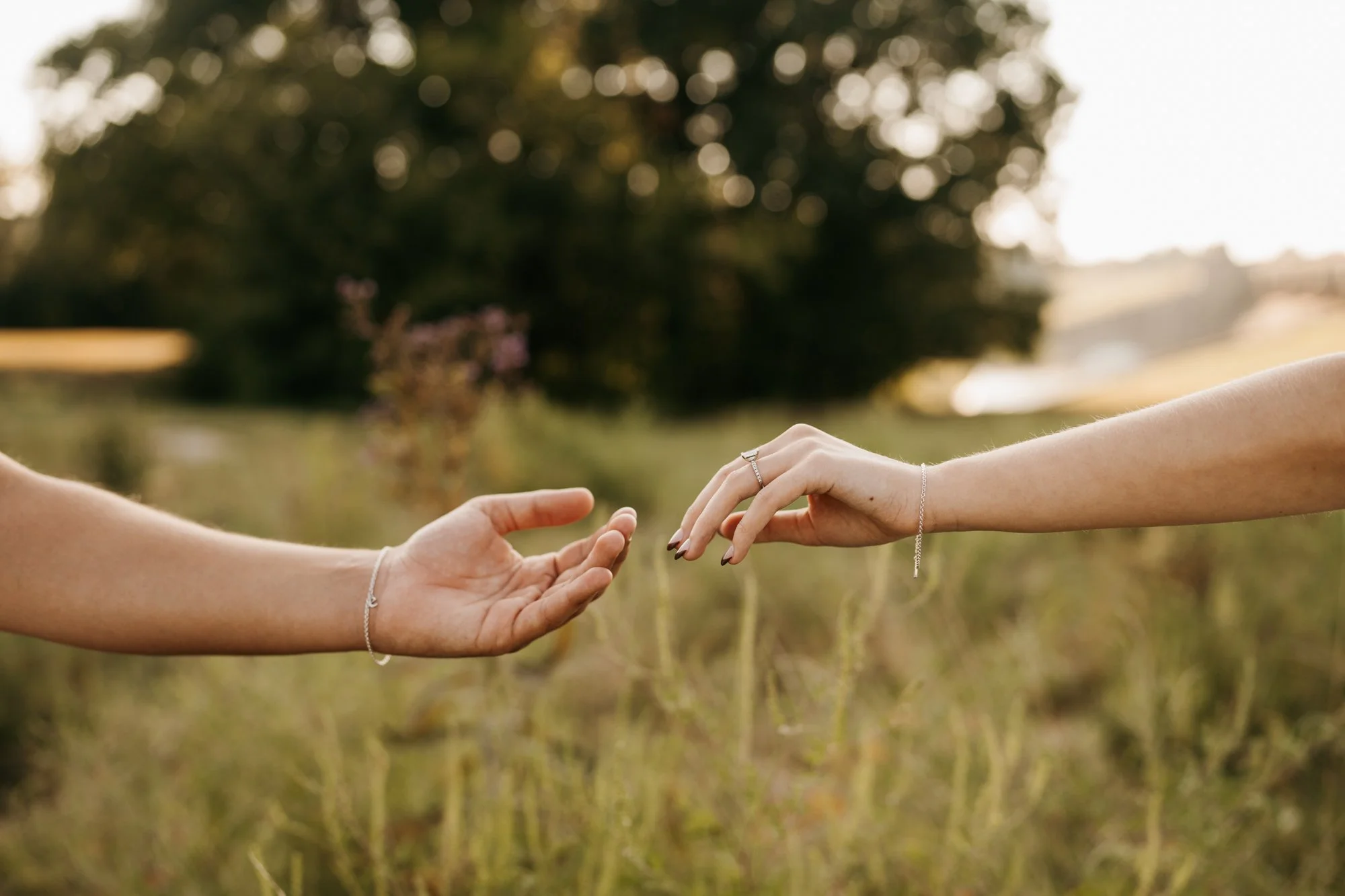 Two hands reaching out towards each other outdoors in a field during daylight.