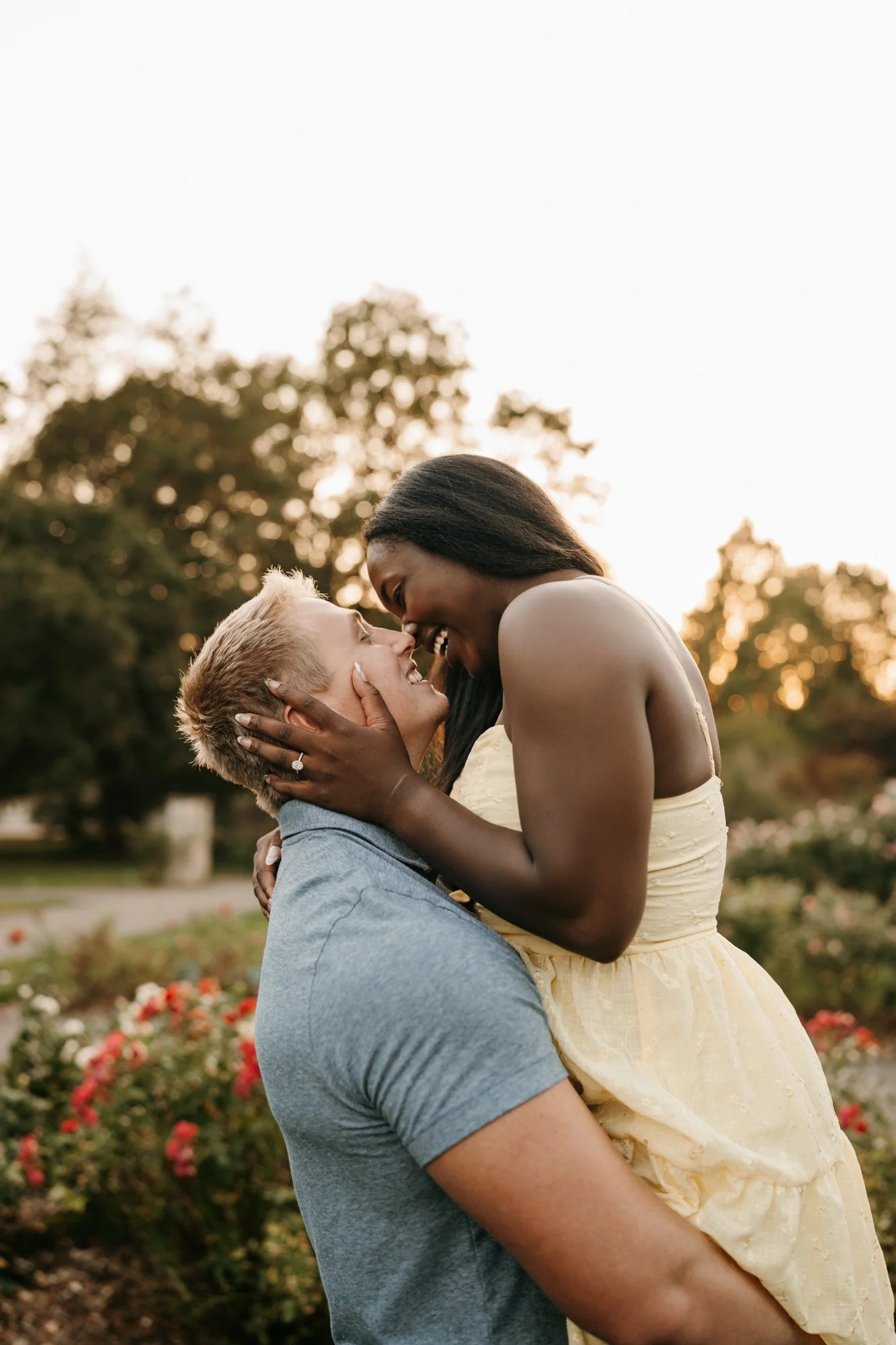 A happy couple sharing an intimate moment outside during sunset, with trees and flowers in the background.