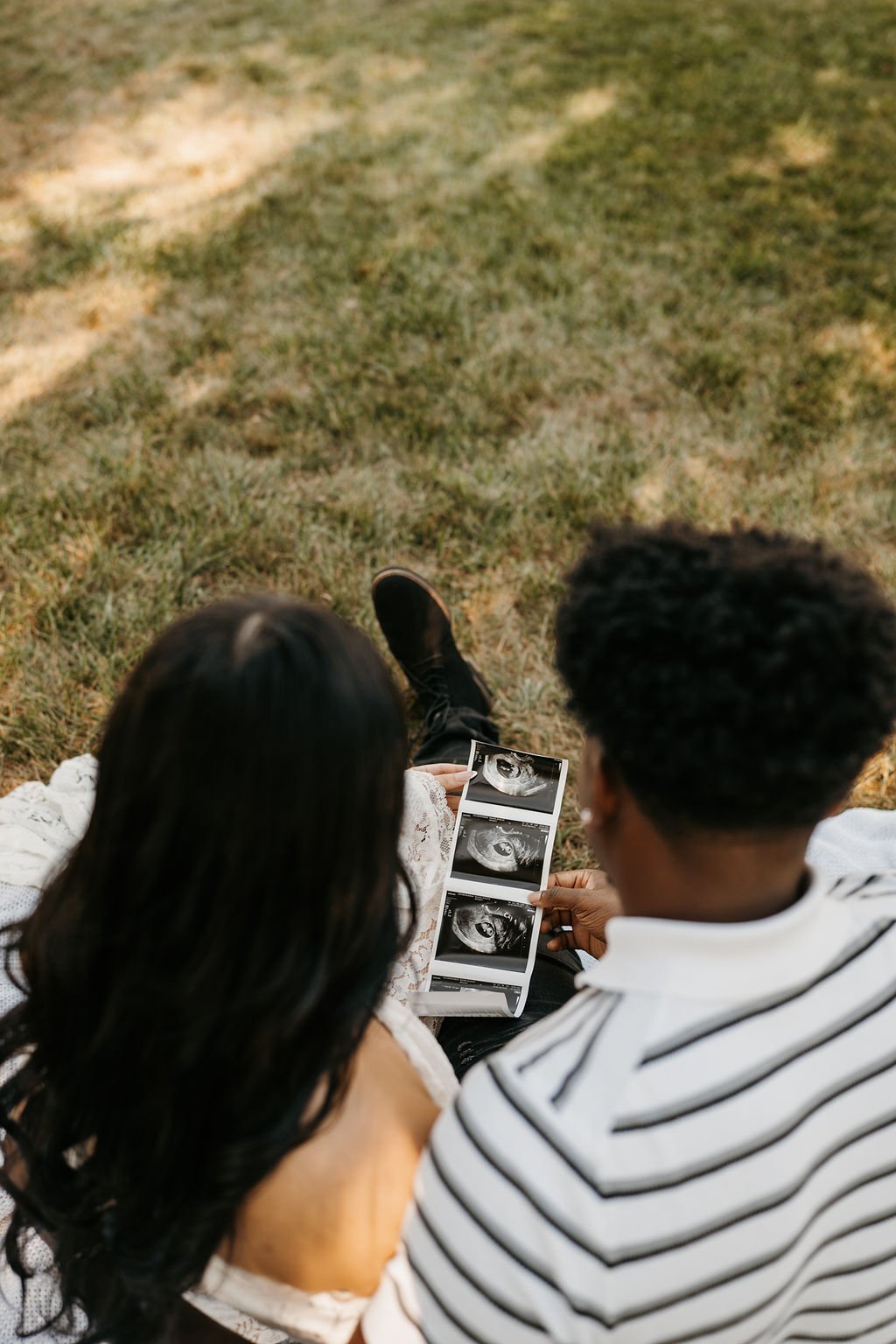 Couple sitting on grass, looking at ultrasound images of a fetus.