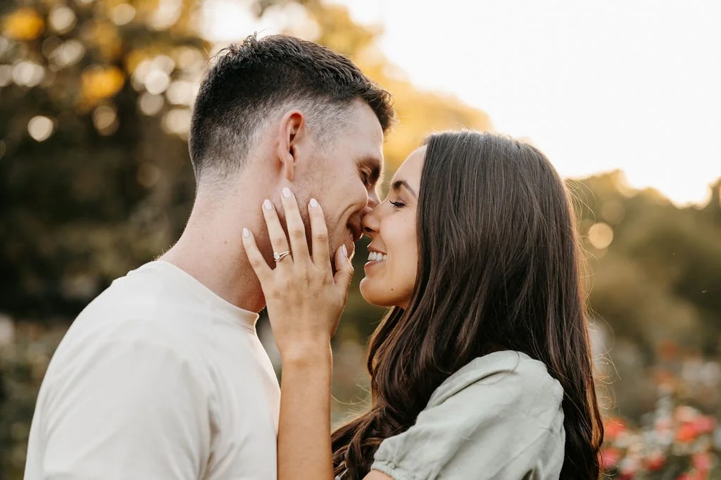 A couple is about to kiss outdoors during sunset, with blurred trees in the background.
