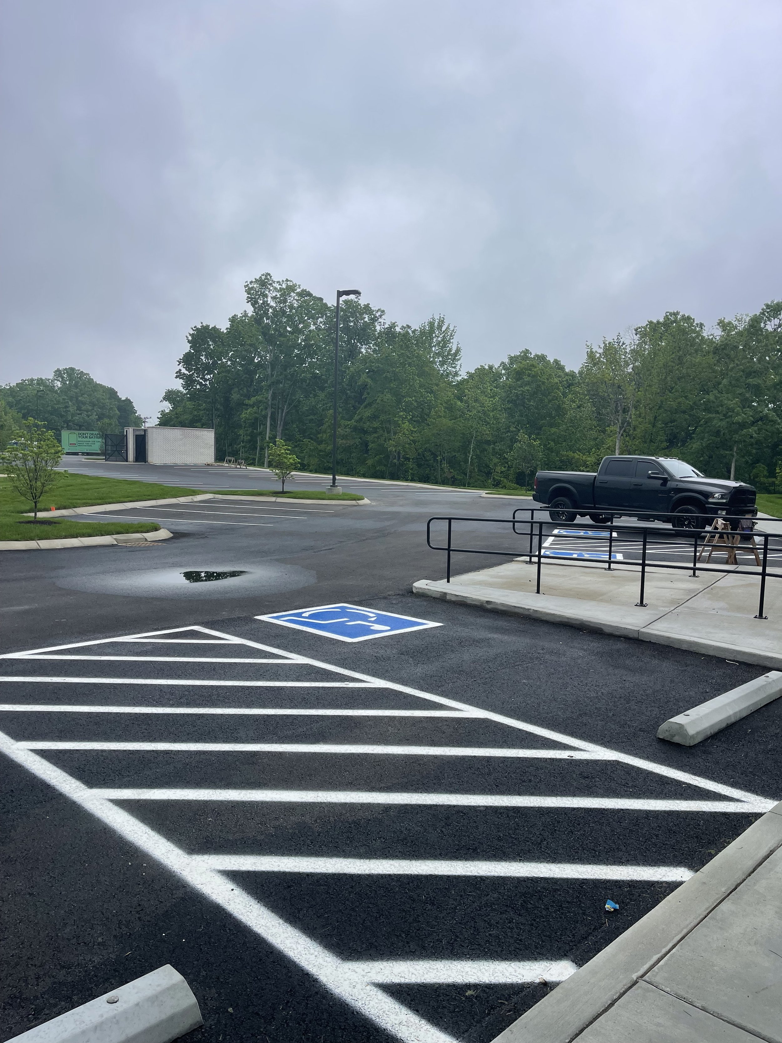 Empty parking lot with a handicap parking space and a wheelchair accessible ramp, cloudy sky, and a black truck parked in the distance.