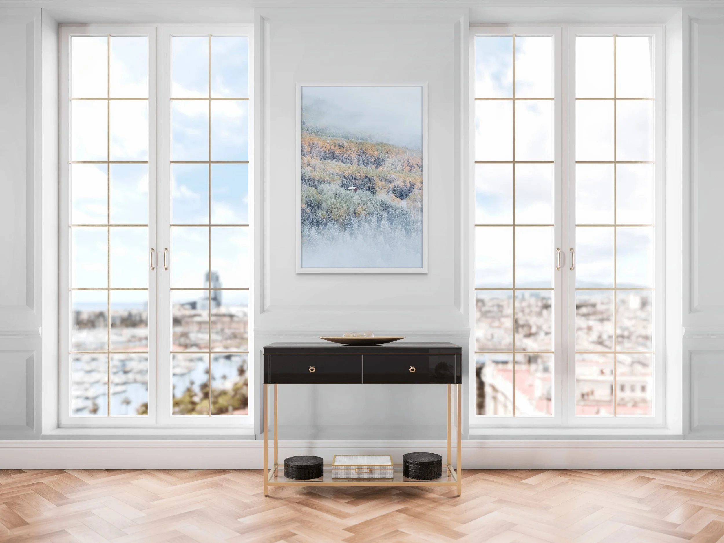 Interior view of a room with three large windows showing cityscape and sky, a black and gold console table, two black round storage boxes, a decorative tray, and a large framed landscape painting of a mountain scene.