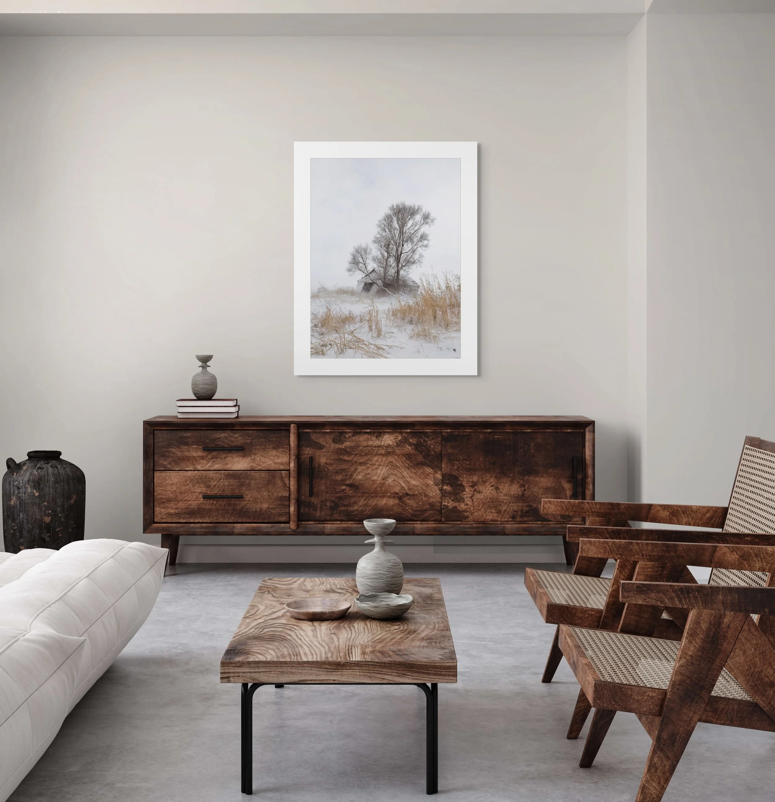 Modern living room with a wooden sideboard, a white sofa, wooden chairs, a wooden coffee table with vases, and a framed winter landscape photograph on the wall.