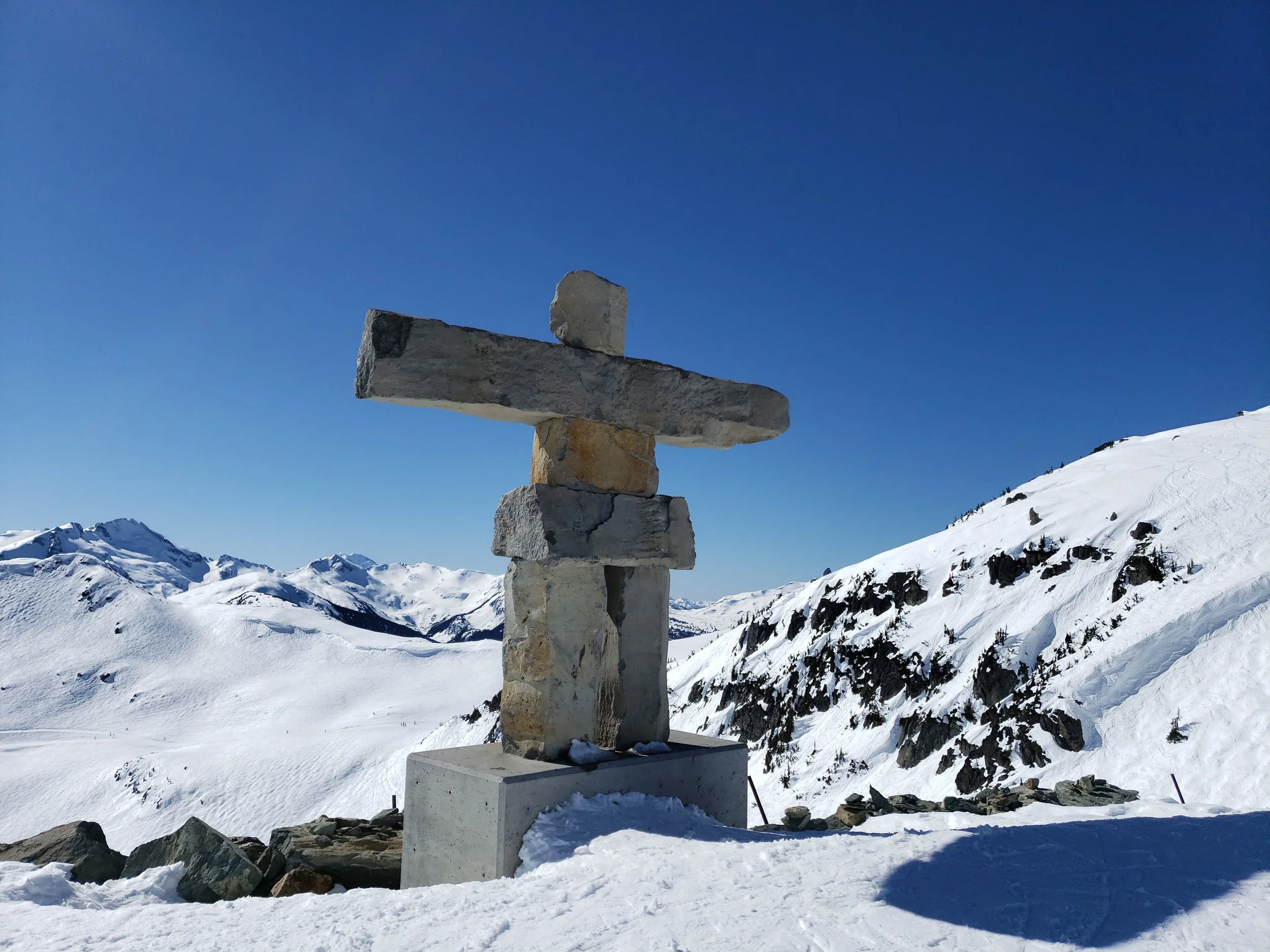 A stone cairn on a snow-covered mountain with a clear blue sky in the background.