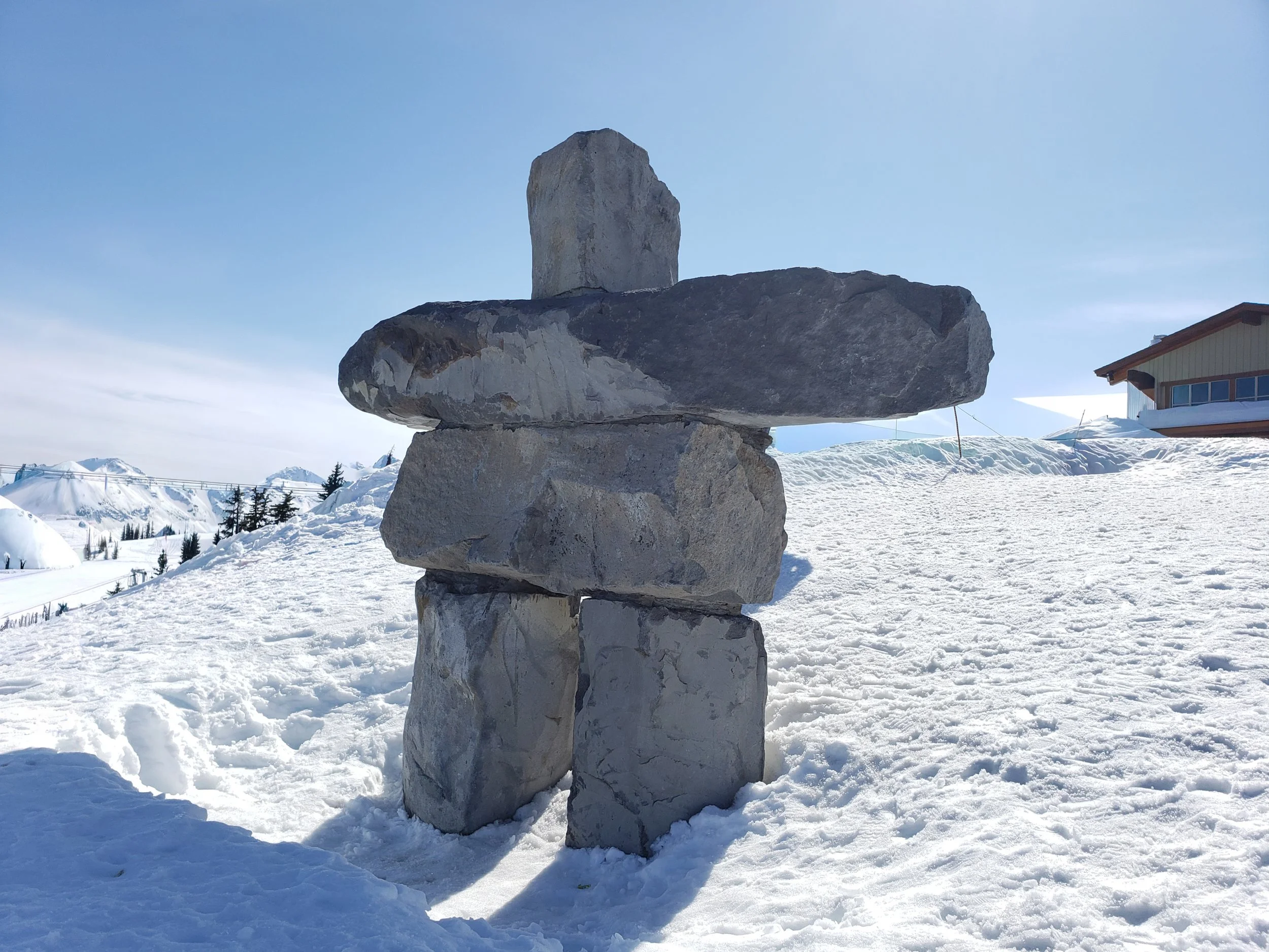 Stacked rocks in a snowy landscape with buildings and mountains in the background.