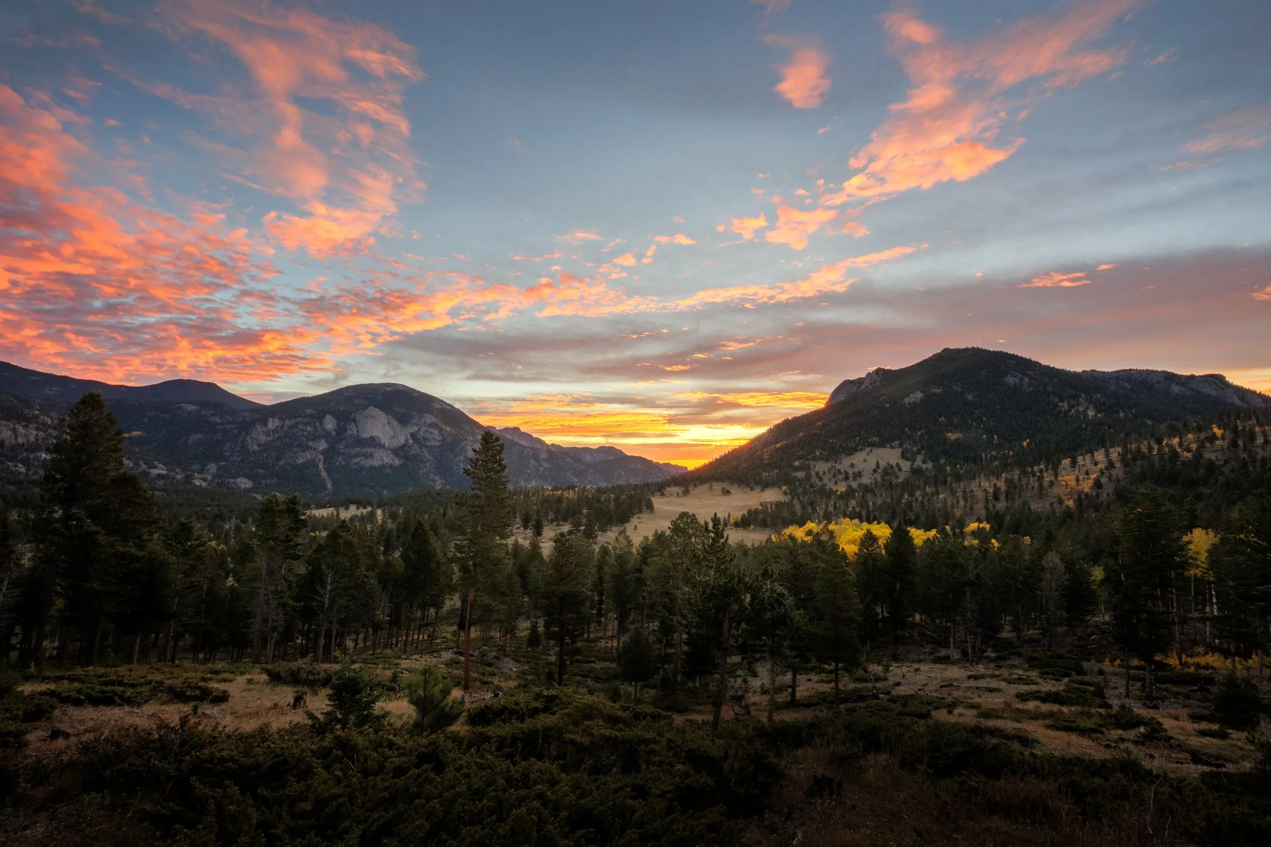 A scenic landscape of mountains, forest, and a colorful sunset sky with clouds