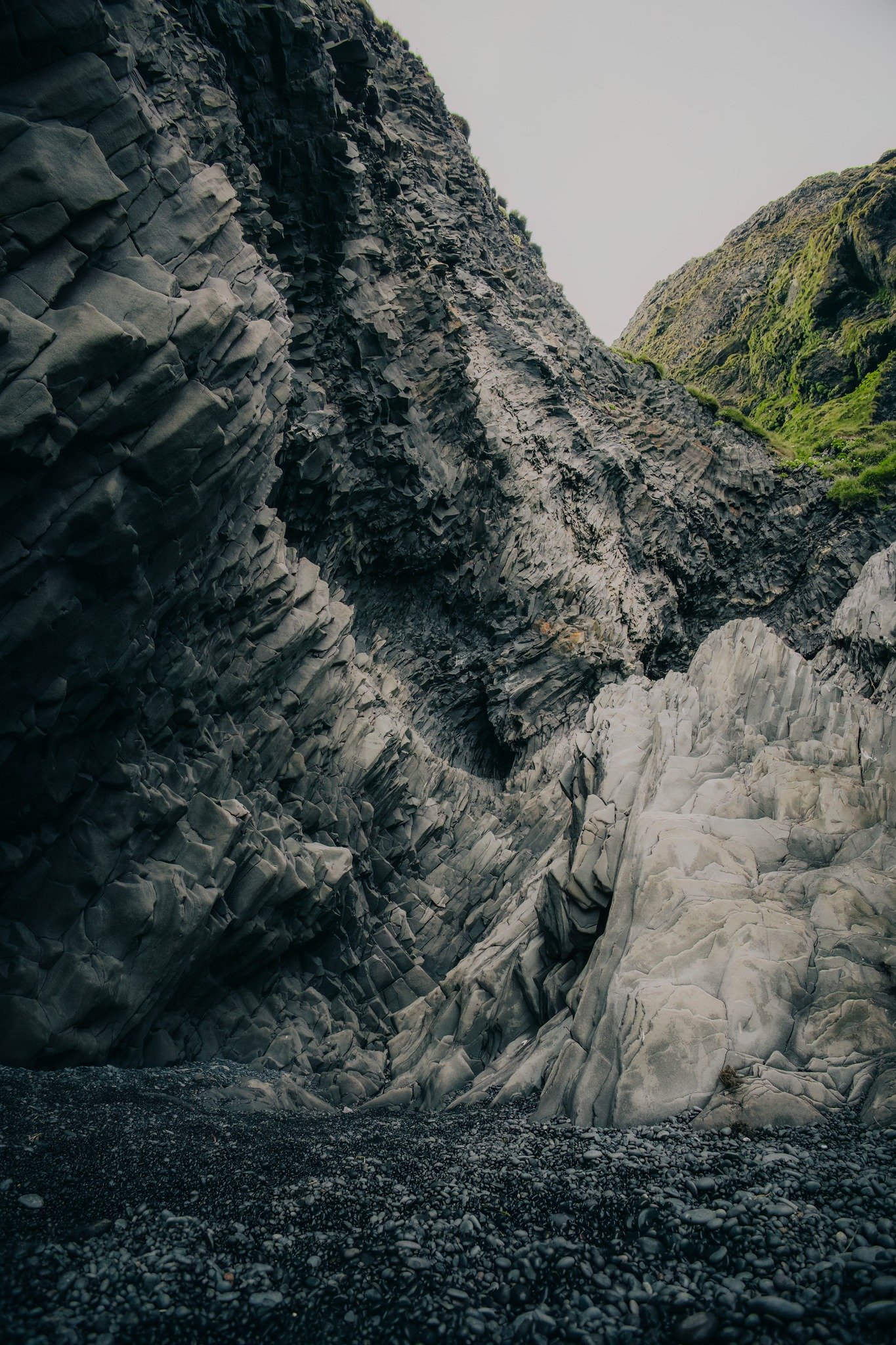 Tall, layered dark gray and light gray rock formations in a narrow canyon with a rocky foreground.