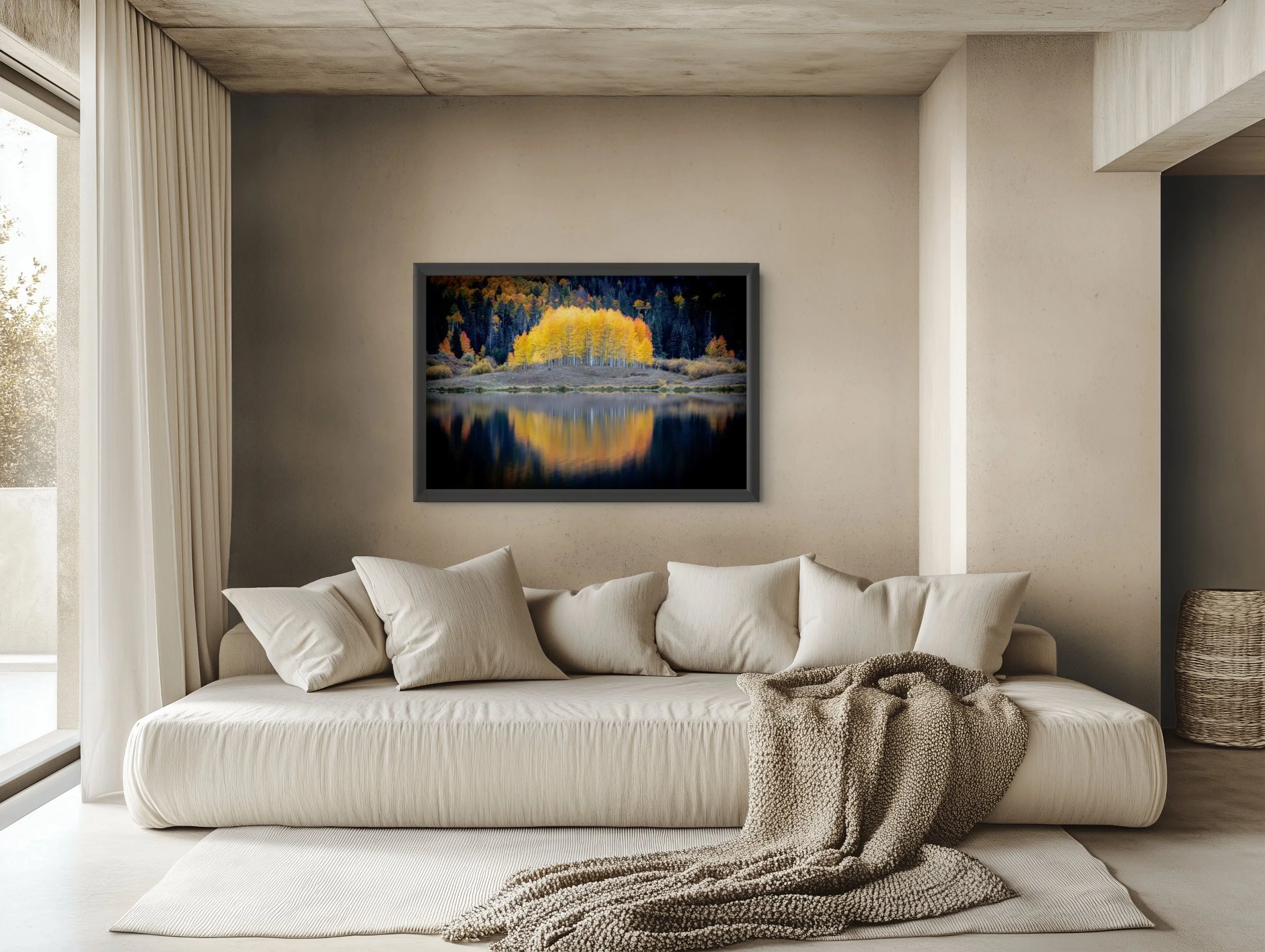A cozy living room with a white sofa adorned with white pillows. A textured beige blanket is draped over the sofa's armrest. Behind the sofa, there is a large scenic landscape painting of colorful trees near a lake, surrounded by a concrete wall with
