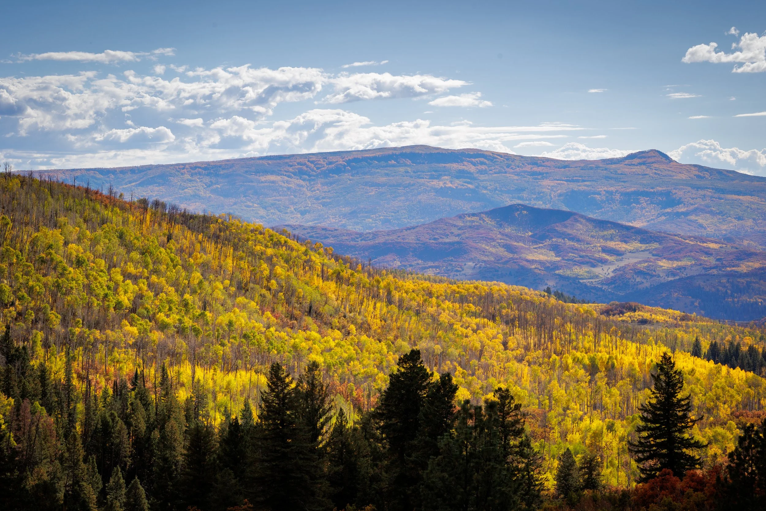 Mountain landscape with colorful autumn trees, partly cloudy sky.