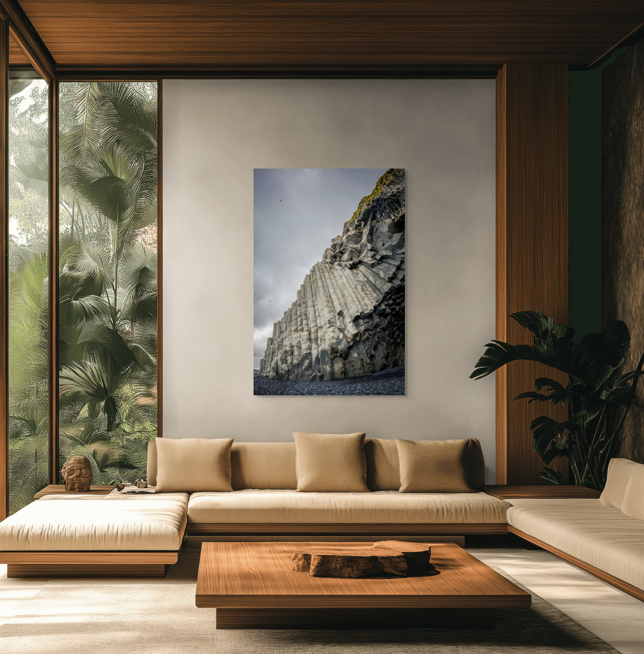 Modern living room with beige sofa, wooden coffee table, large wall art of a rocky cliff, indoor plants, and large windows overlooking greenery.
