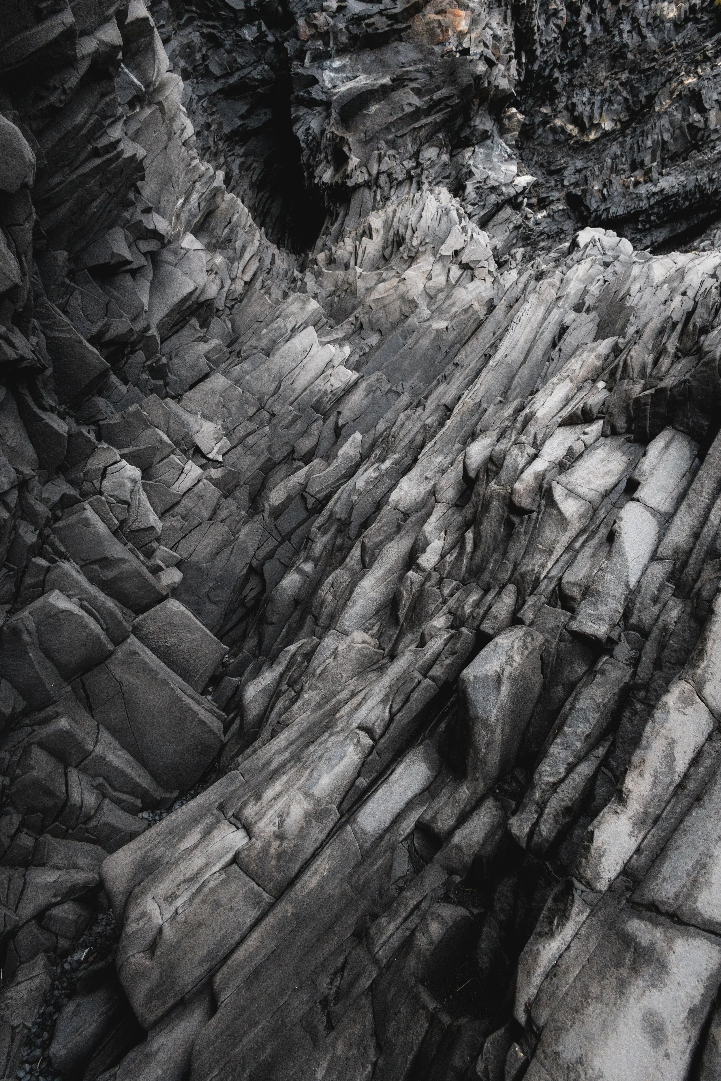 Close-up of jagged, layered gray rocks in a canyon or crevice, with dark shadows and a narrow opening at the top.