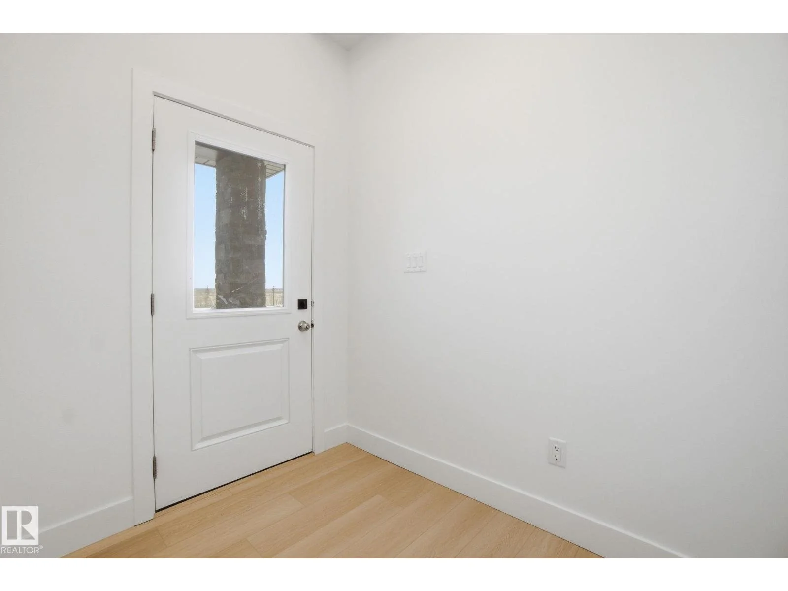 Empty white room with a door and a window, showing a brick column outside