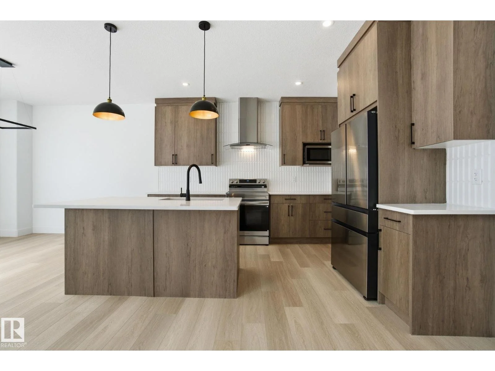 Modern kitchen with wooden cabinetry, black appliances, white island countertop, and pendant lighting.