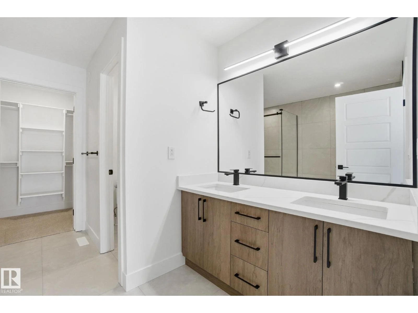 Bathroom vanity with double sinks, black fixtures, large mirror, and a separate shower area with glass door in a modern bathroom.