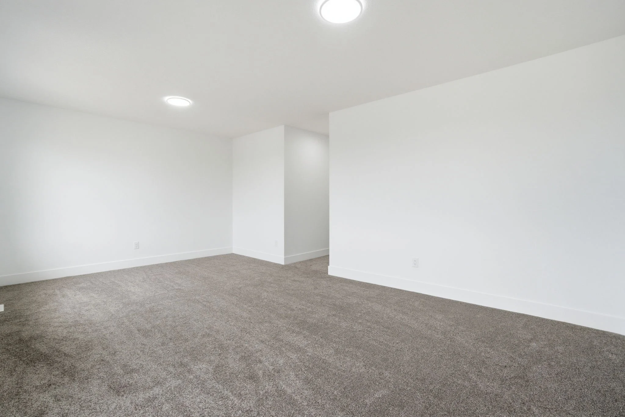 Empty room with white walls, beige carpet, and ceiling lights.