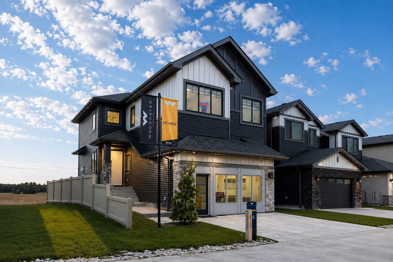 Modern three-story house with black and white exterior, front yard, and driveway, under partly cloudy sky.