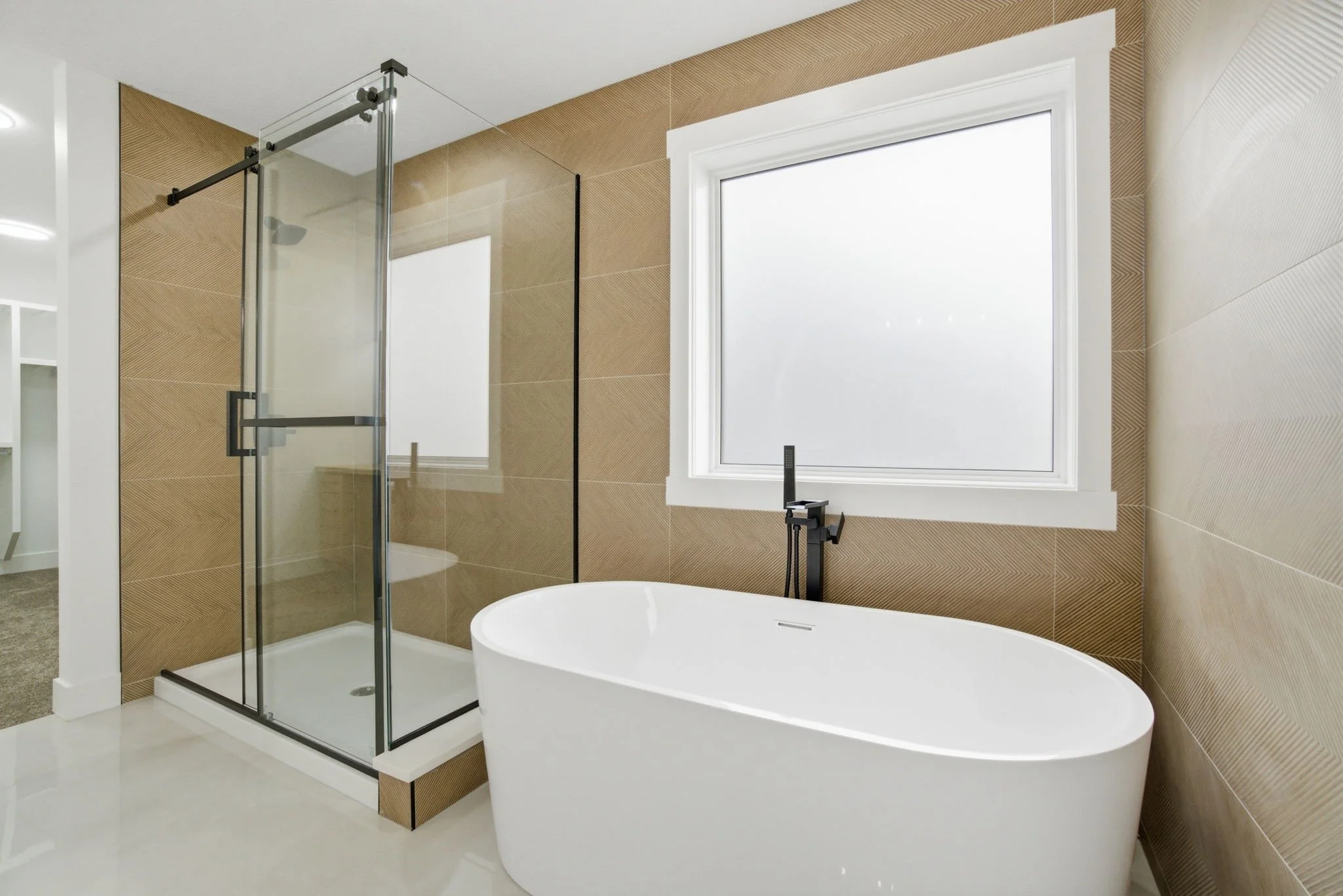 Modern bathroom with a glass shower enclosure, a freestanding bathtub, a large window, and neutral-colored walls and floor.