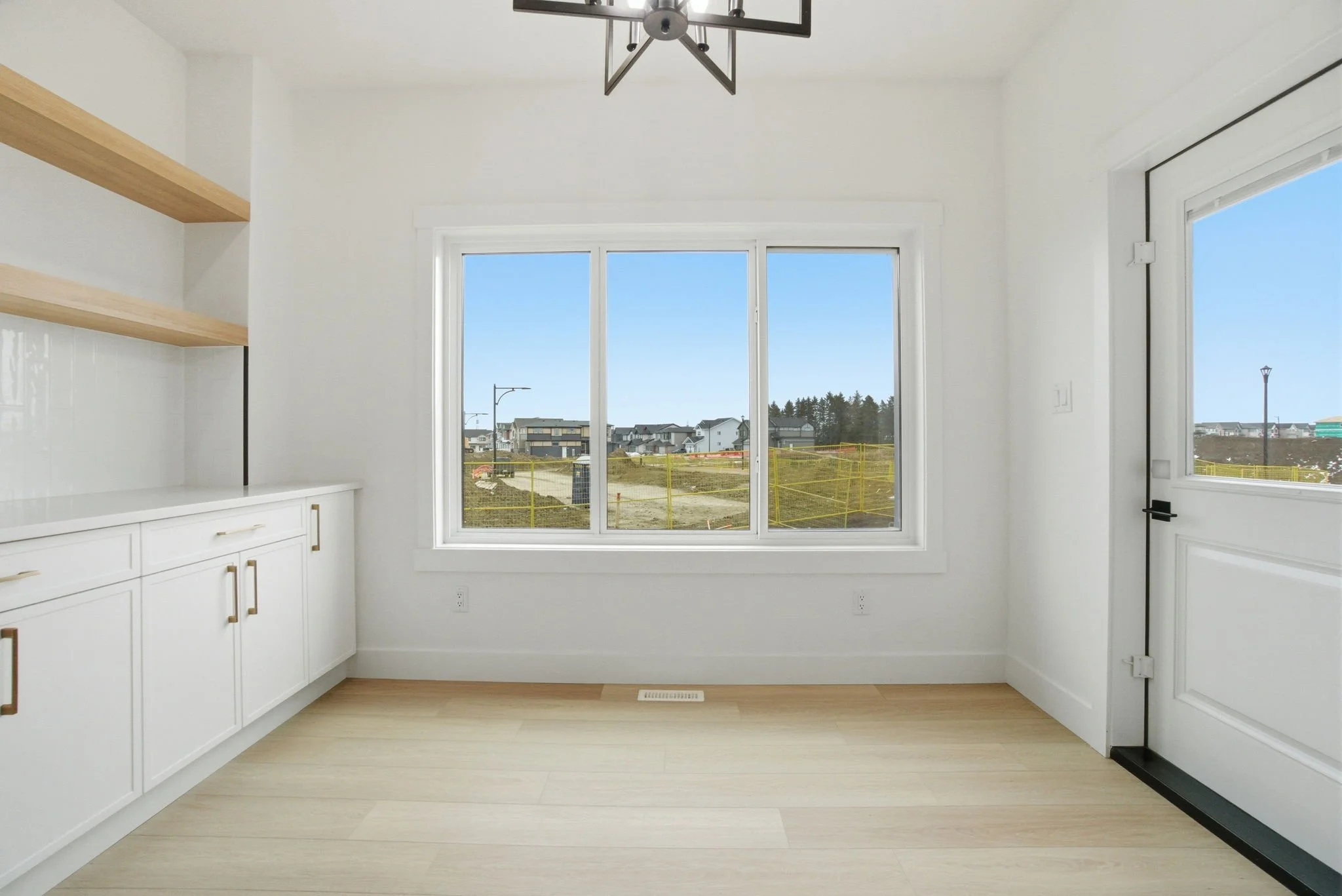 Empty modern kitchen with large windows looking out onto a residential street with construction fencing.
