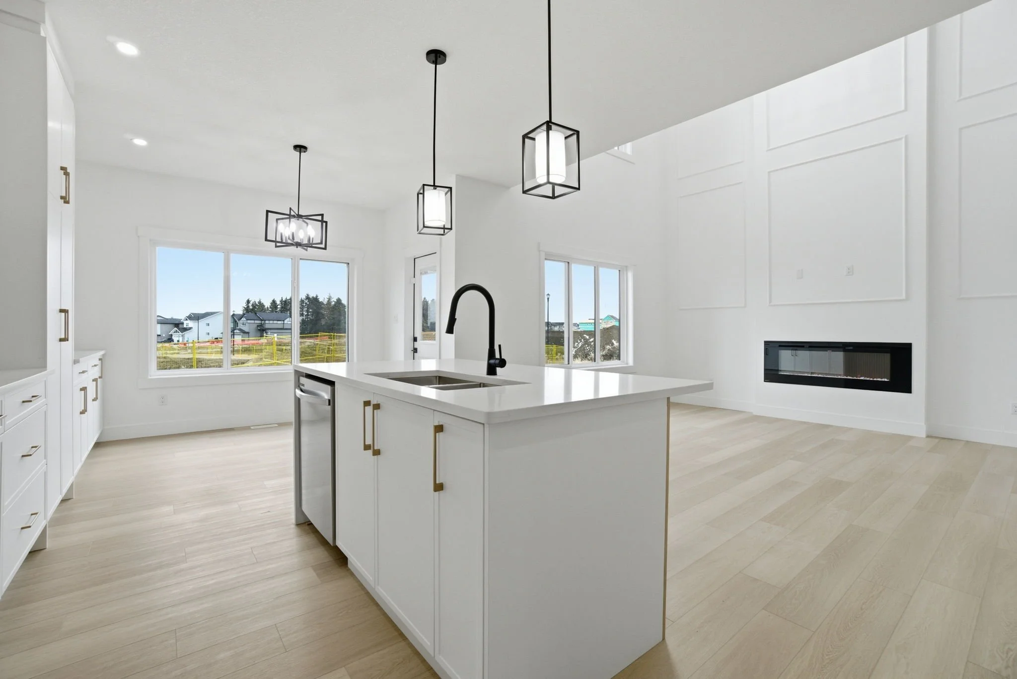 Modern kitchen with white cabinets, an island with a black faucet, pendant lights, large windows, and a built-in fireplace.