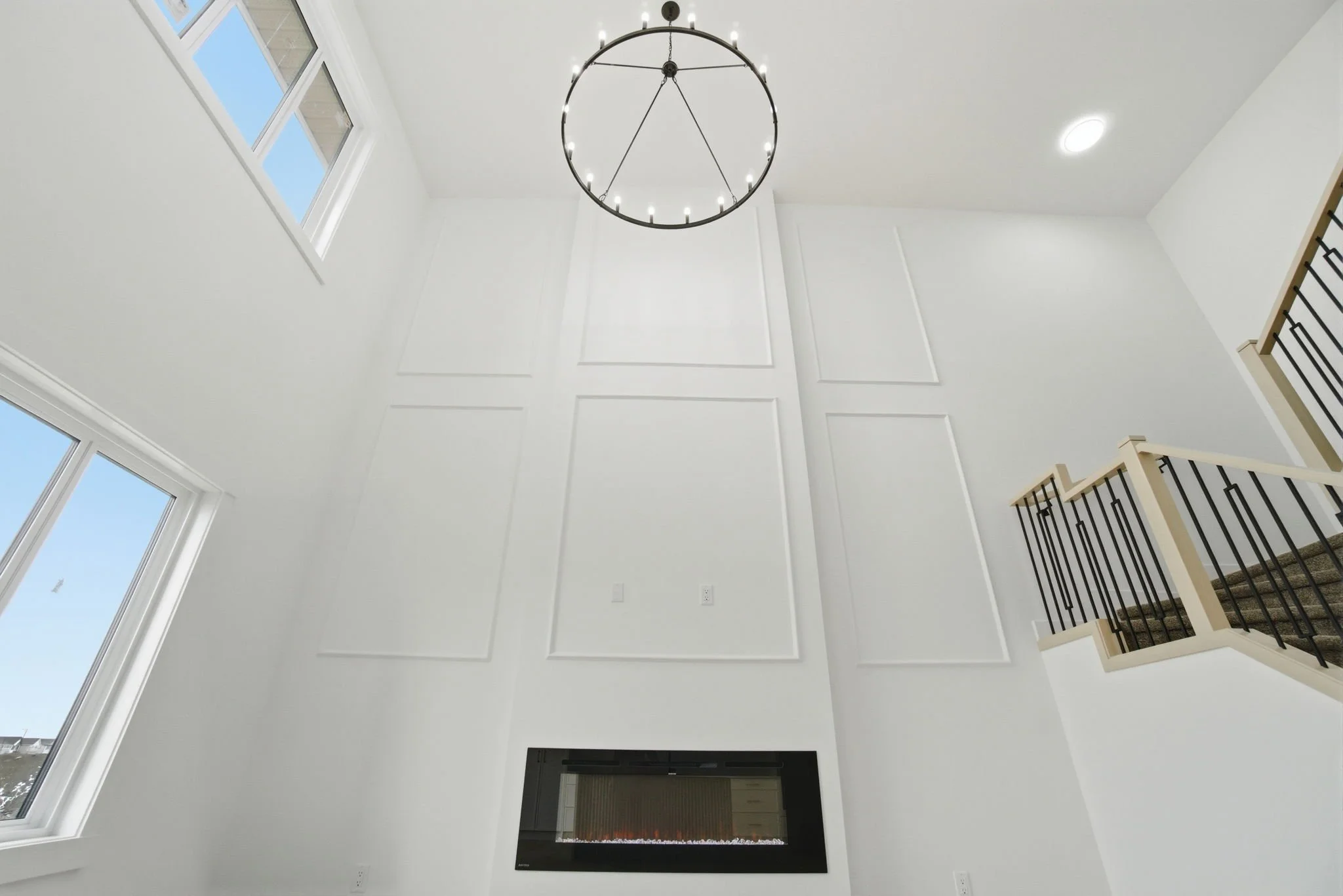 View of a high ceiling with large windows, a modern circular chandelier, and a fireplace below.