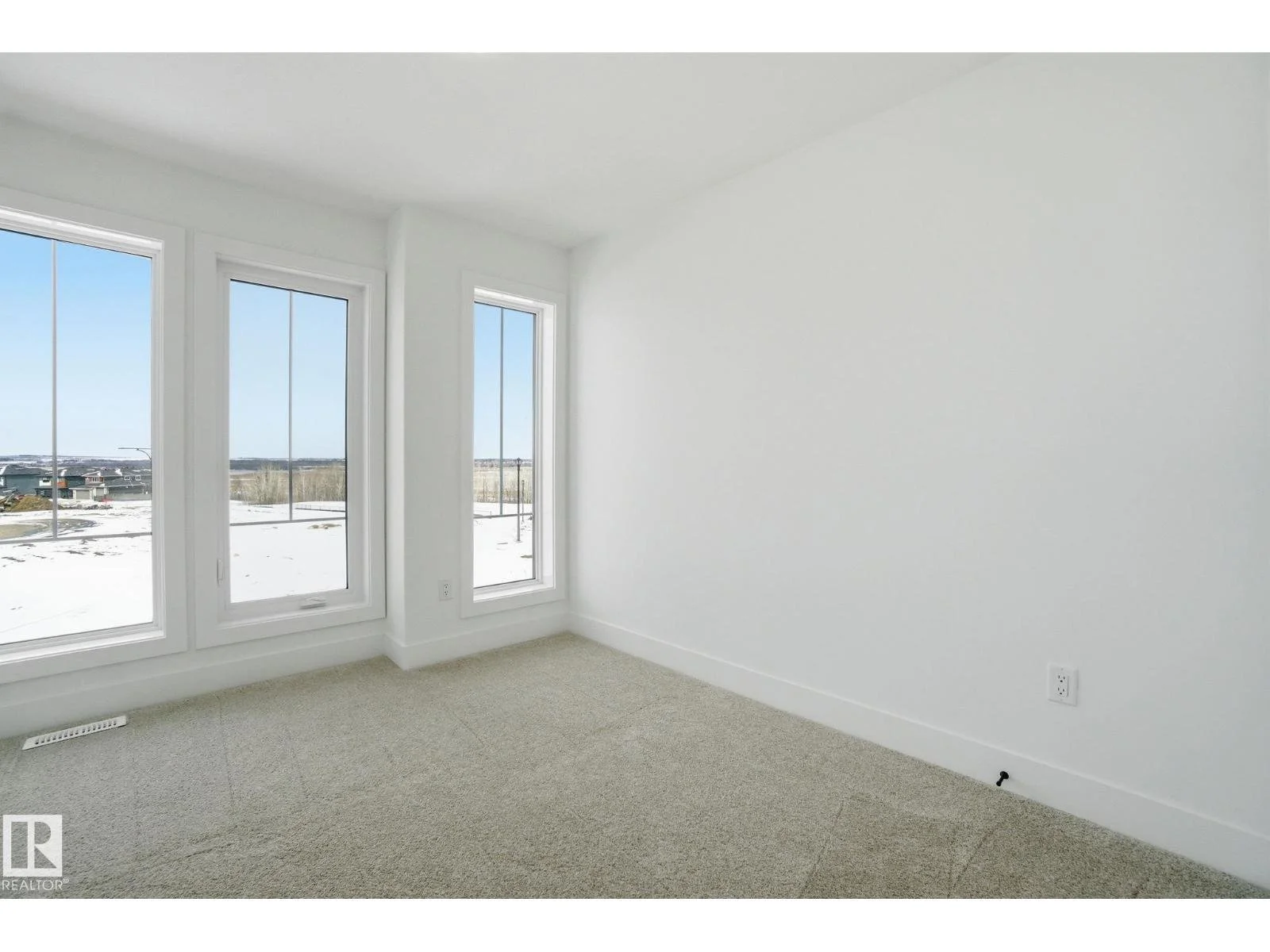 Empty white room with three large windows showing a snowy outdoor landscape.